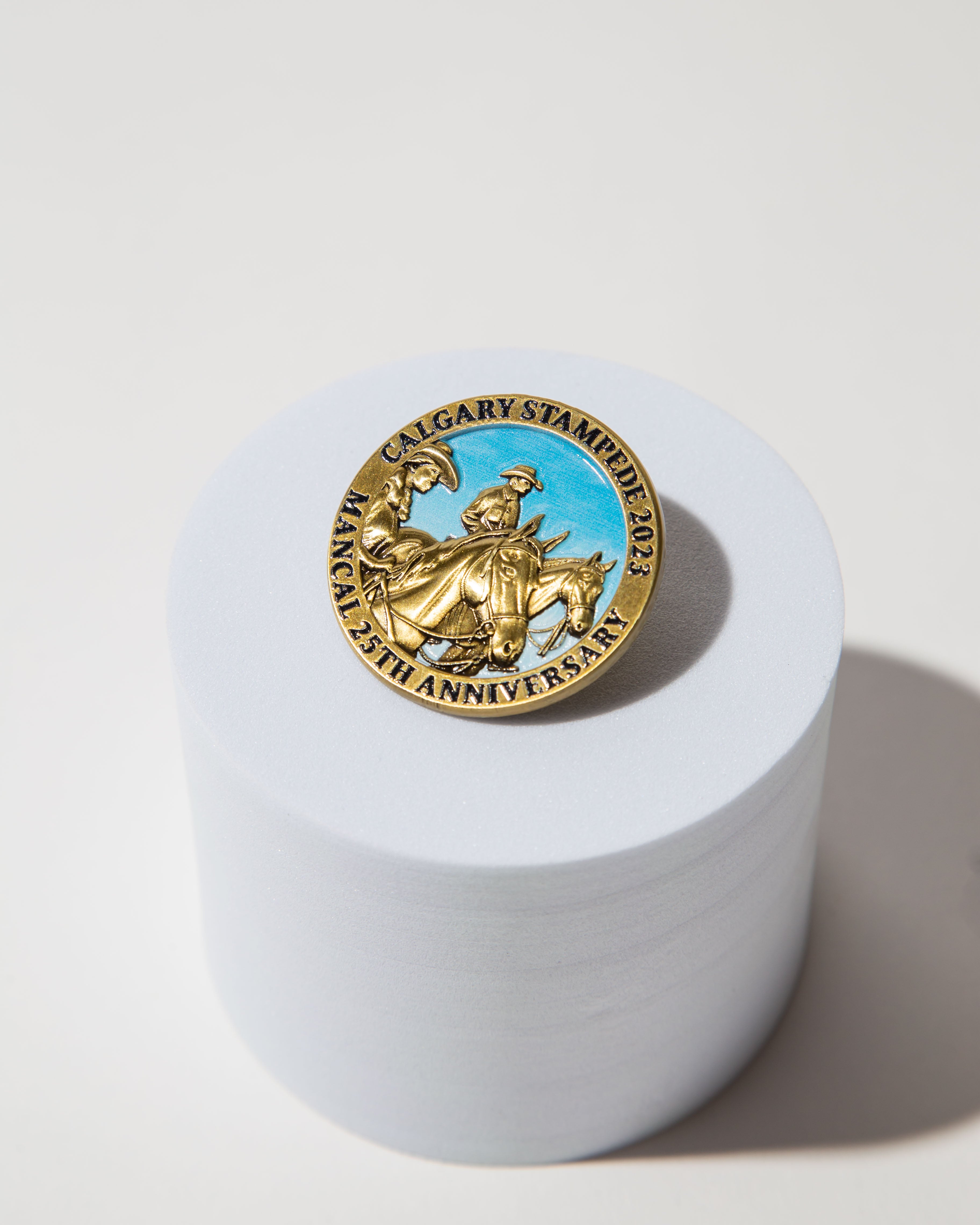 Gold Calgary Stampede 2023 25th anniversary pin with cowboy design on a white cylindrical stand.