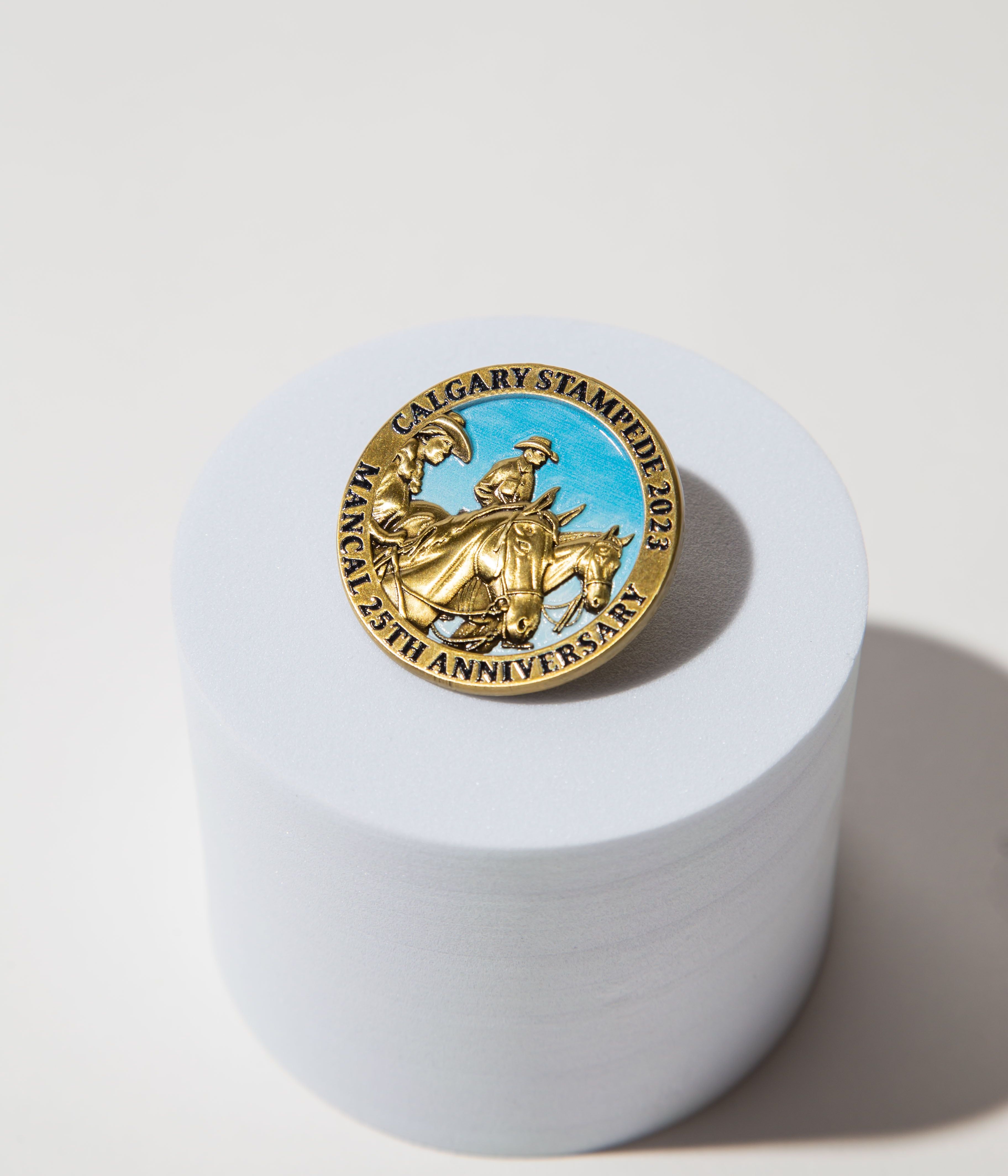 Gold Calgary Stampede 2023 25th anniversary pin with cowboy design on a white cylindrical stand.
