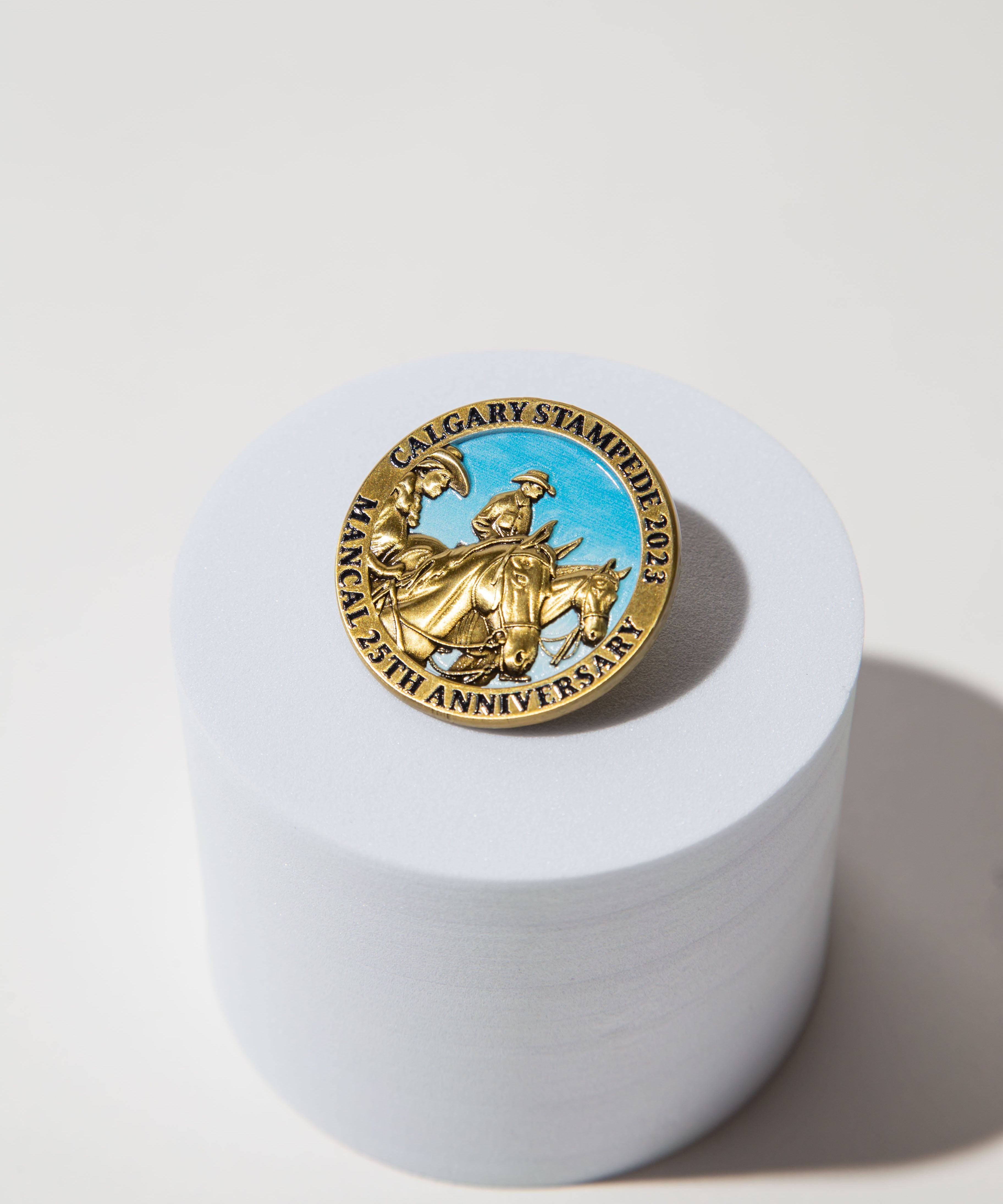 Gold Calgary Stampede 2023 25th anniversary pin with cowboy design on a white cylindrical stand.