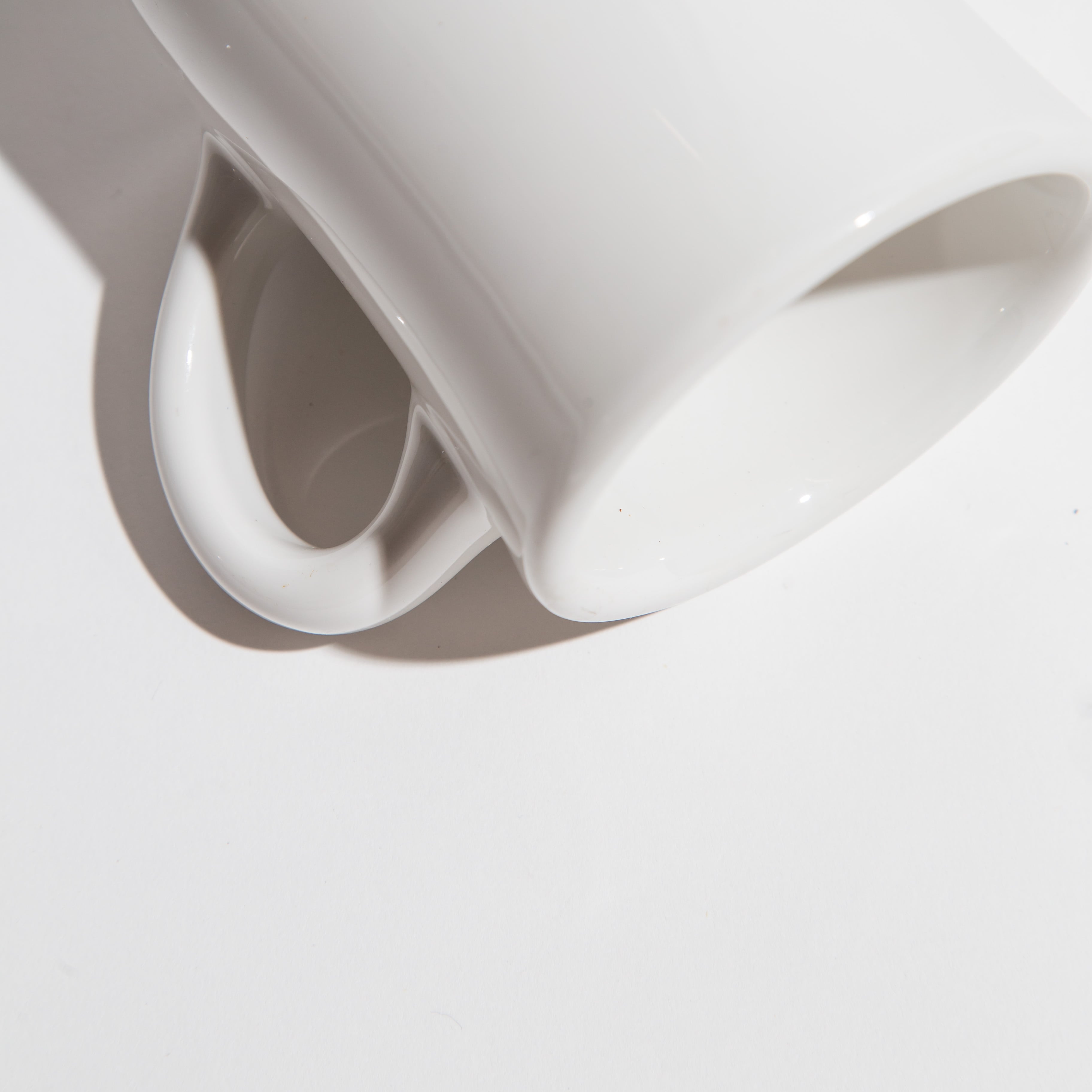 Close-up of a white ceramic mug lying on its side with a shadow cast on a white surface.