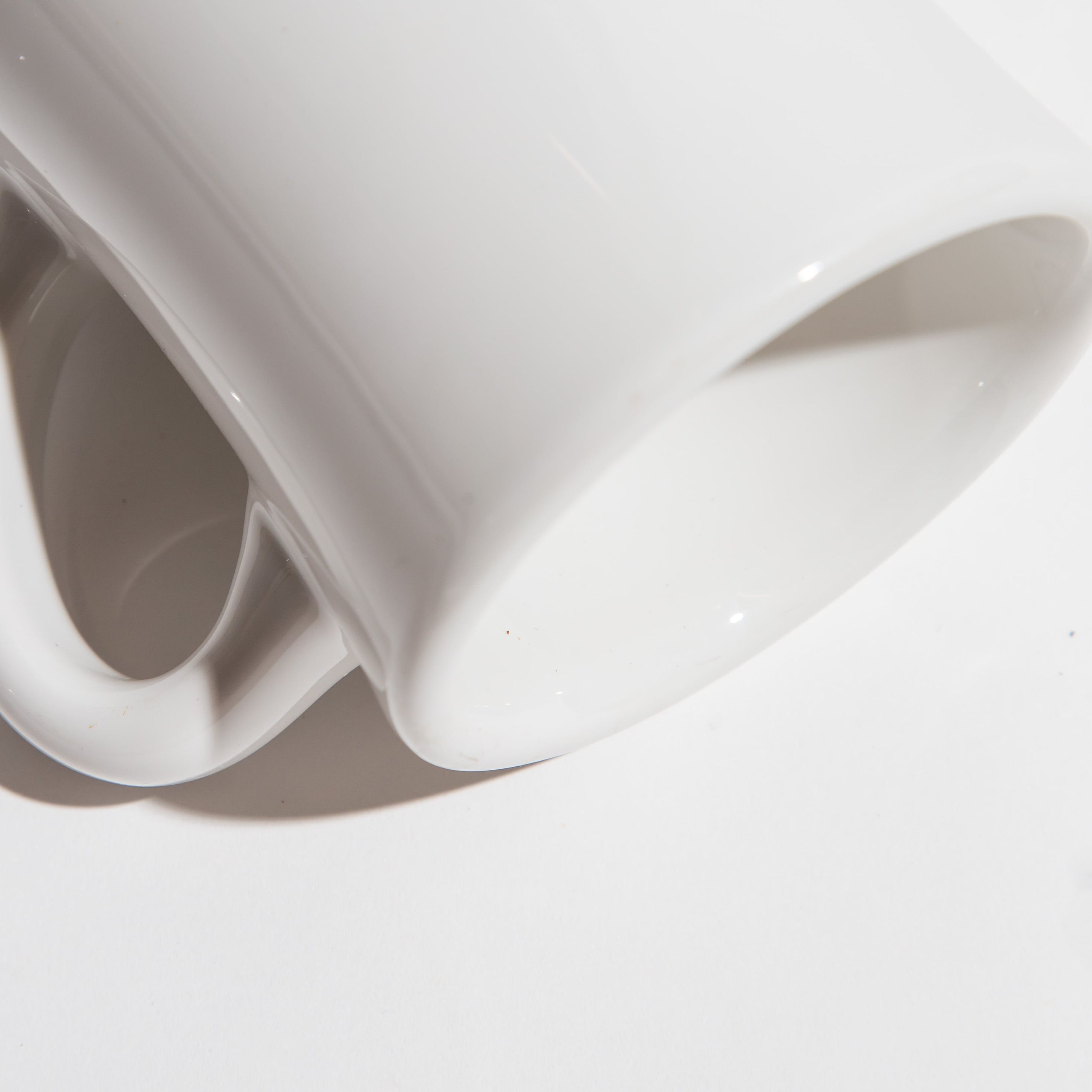 Close-up of a white ceramic mug lying on its side with a shadow cast on a white surface.