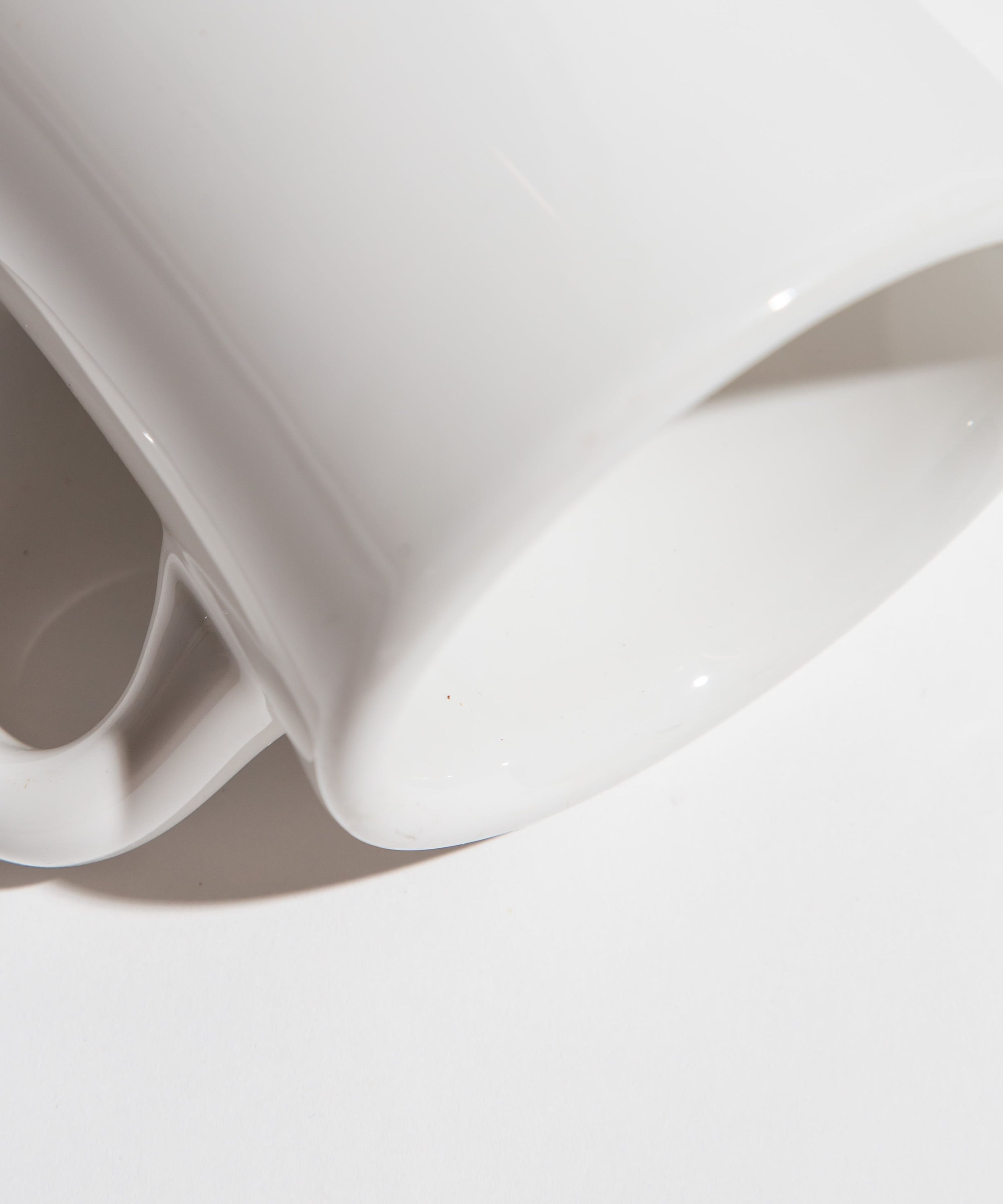 Close-up of a white ceramic mug lying on its side with a shadow cast on a white surface.