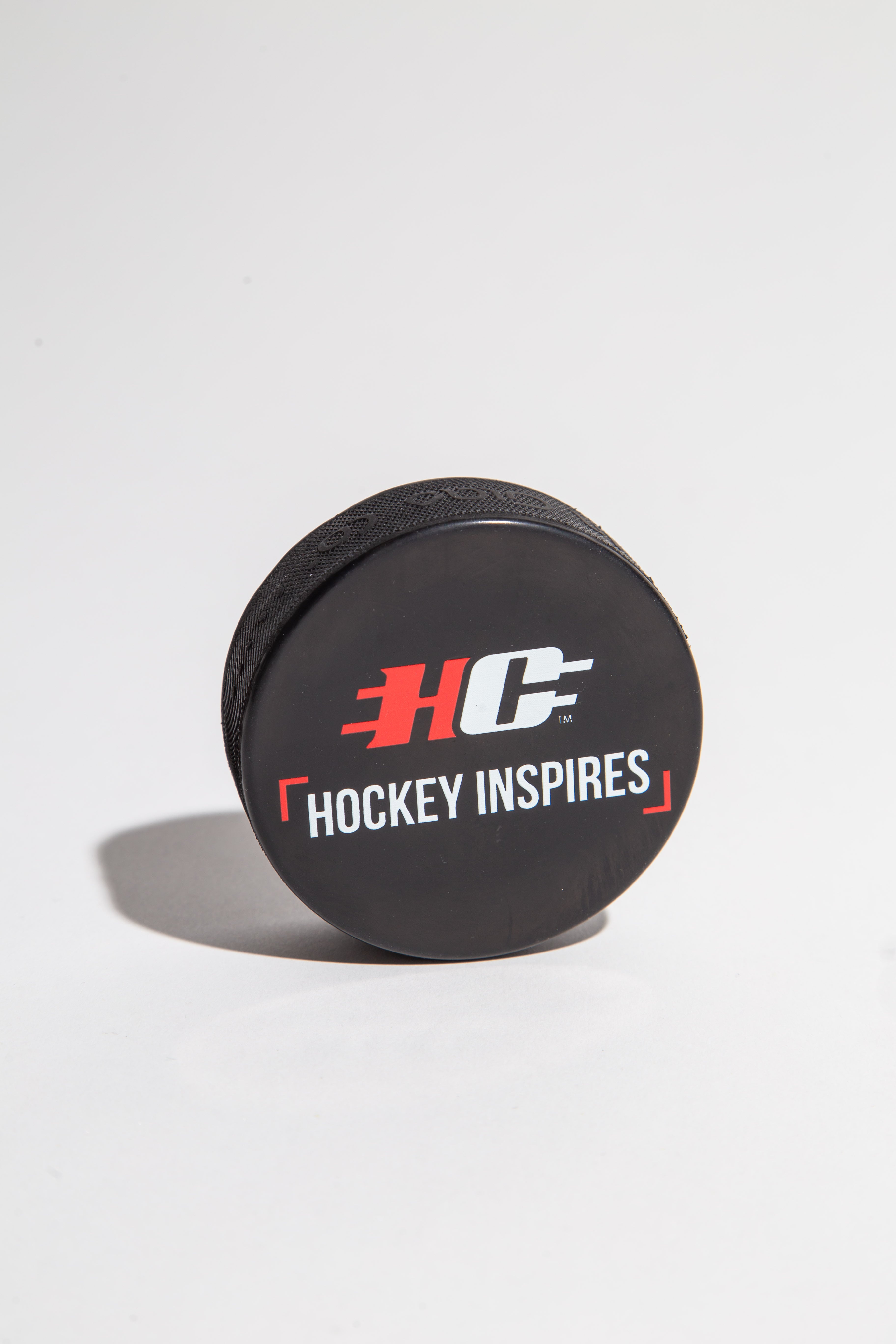 Black hockey puck with 'Hockey Inspires' logo on a white background.