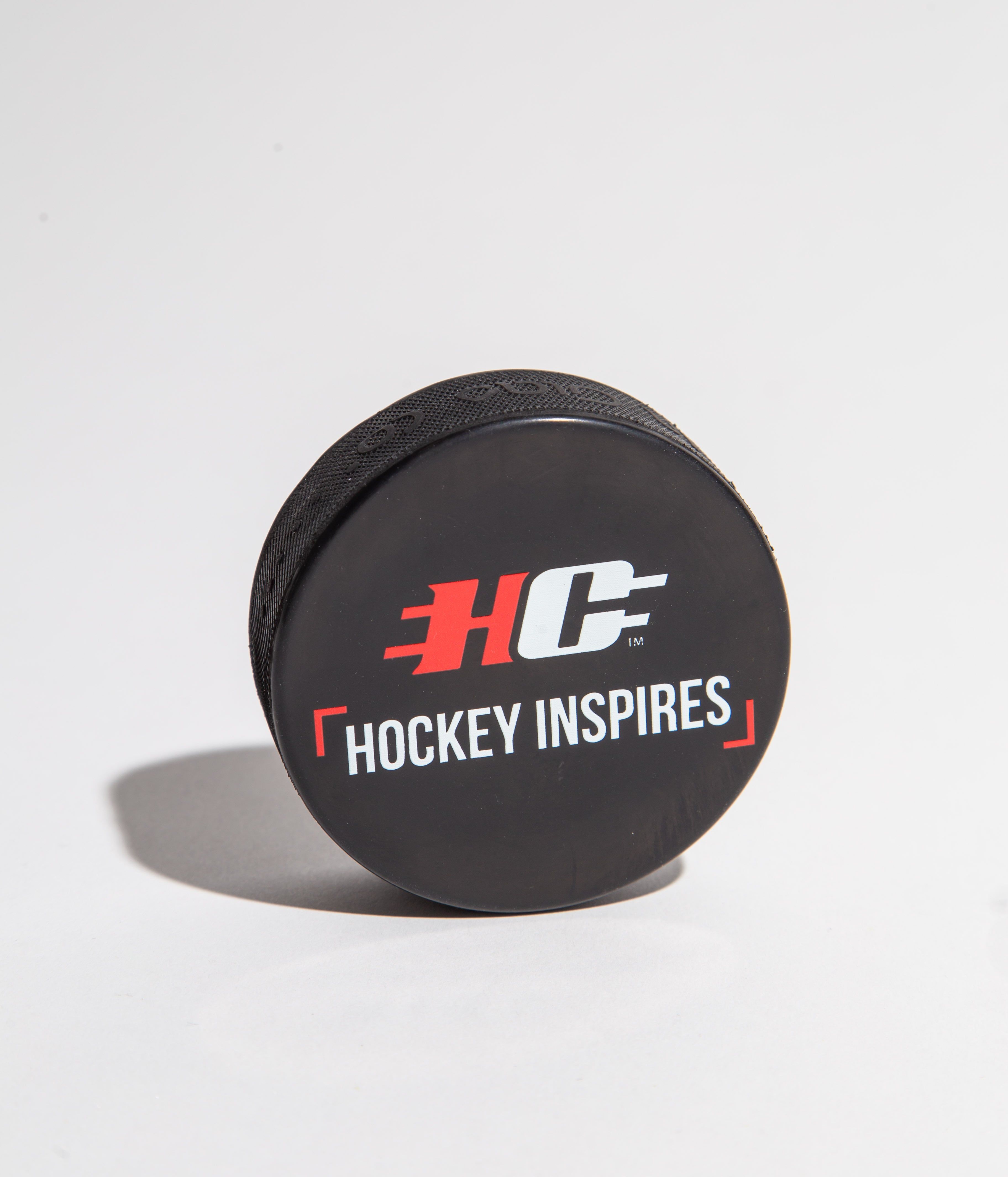 Black hockey puck with 'Hockey Inspires' logo on a white background.