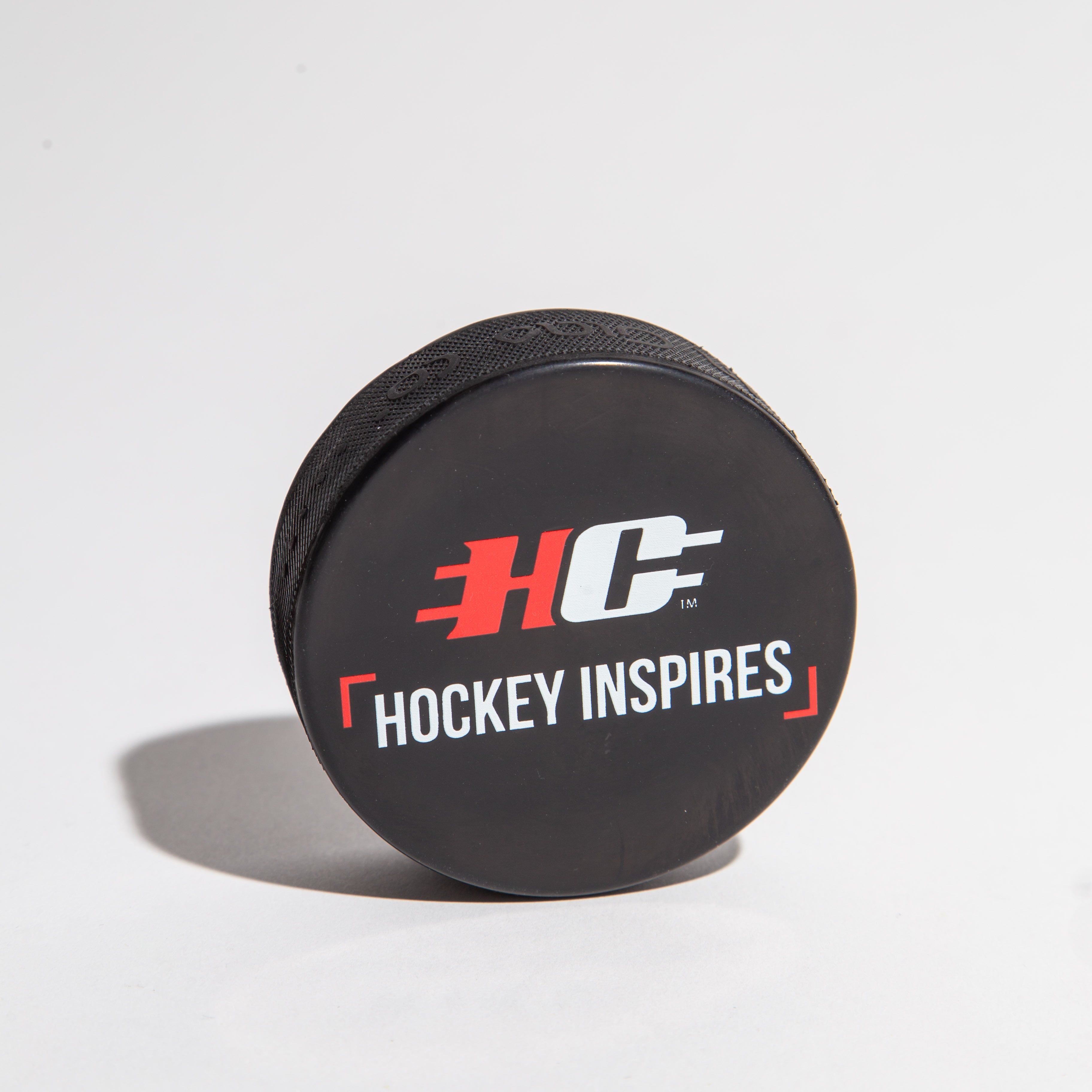 Black hockey puck with 'Hockey Inspires' logo on a white background.