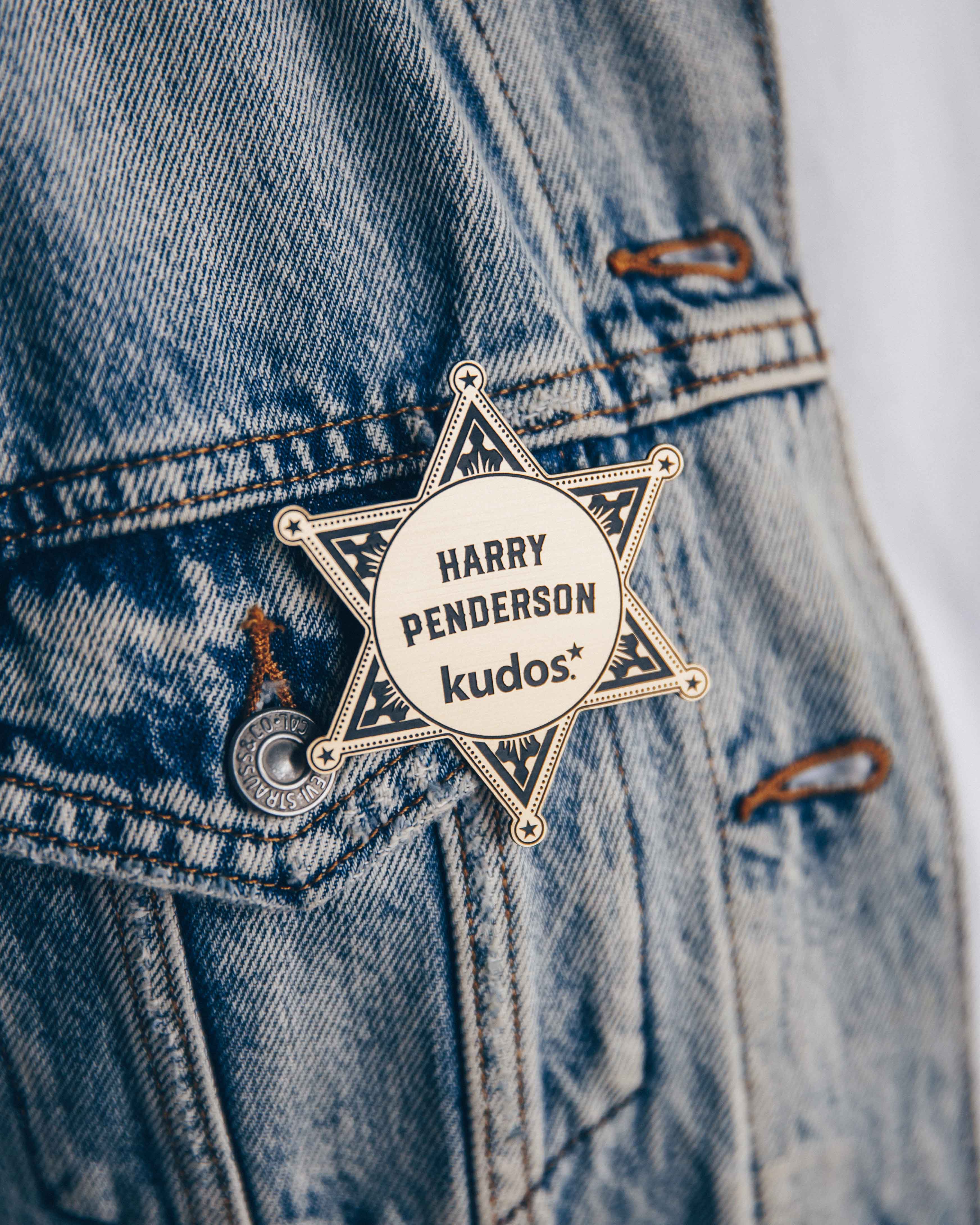 Close-up of a star-shaped badge on a denim jacket with the name 'Harry Penderson' and 'kudos'.