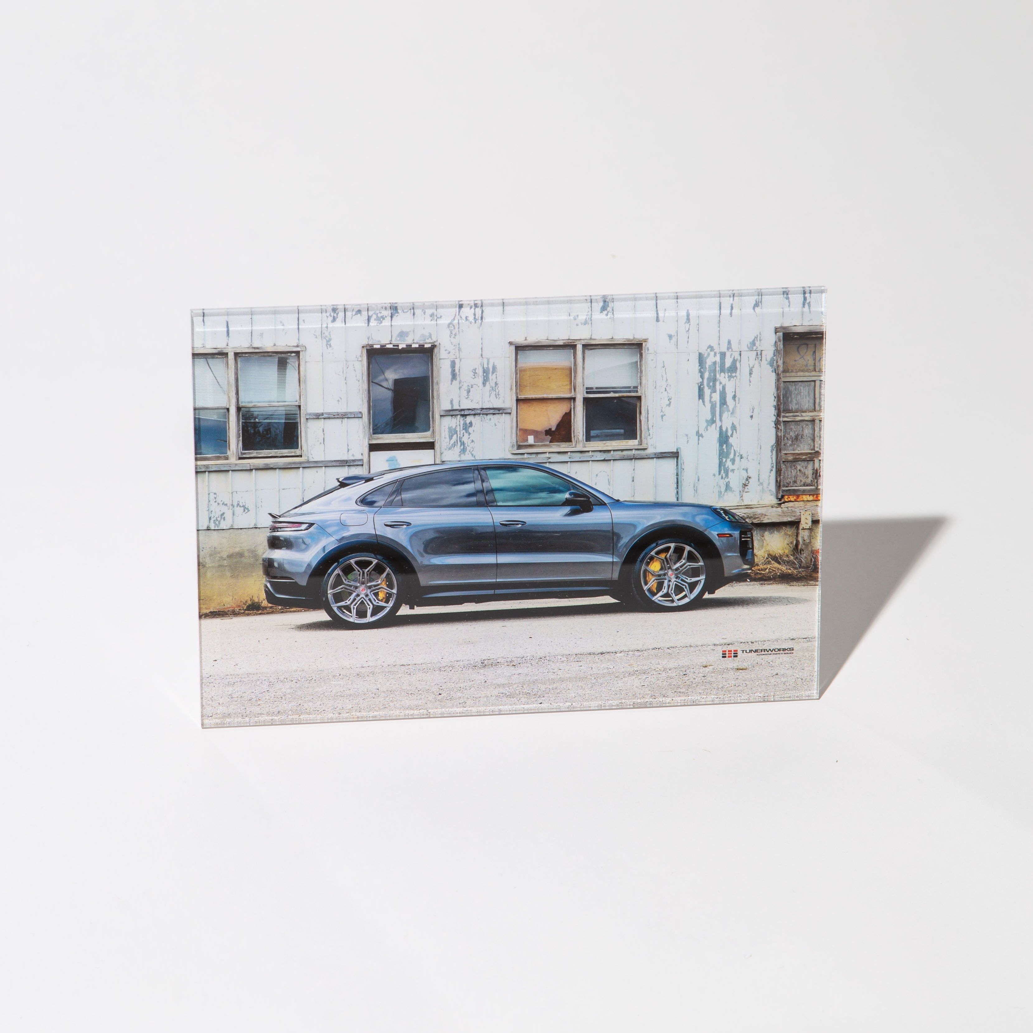 Blue Porsche Cayenne SUV parked in front of a weathered industrial building with large windows.