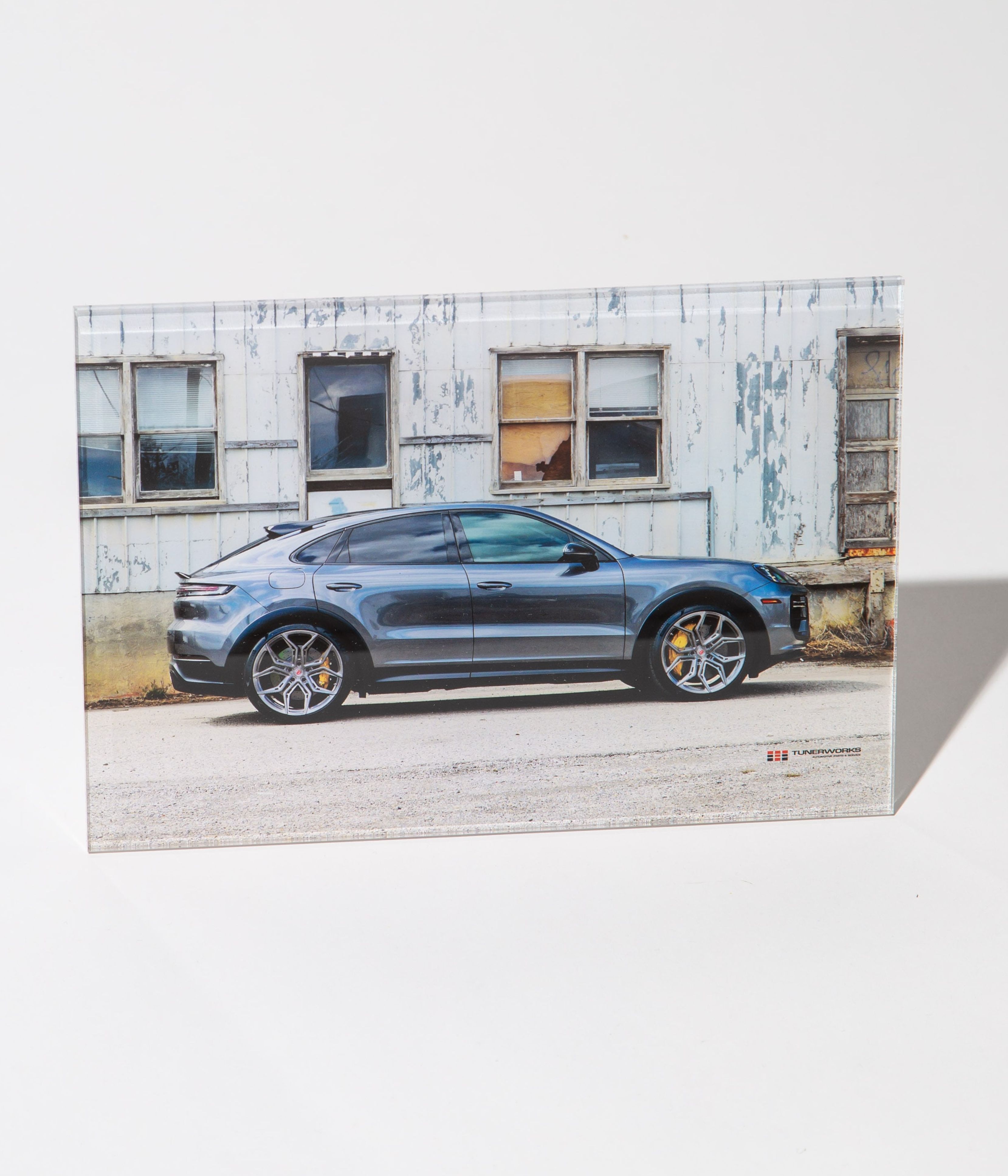 Blue Porsche Cayenne SUV parked in front of a weathered industrial building with large windows.