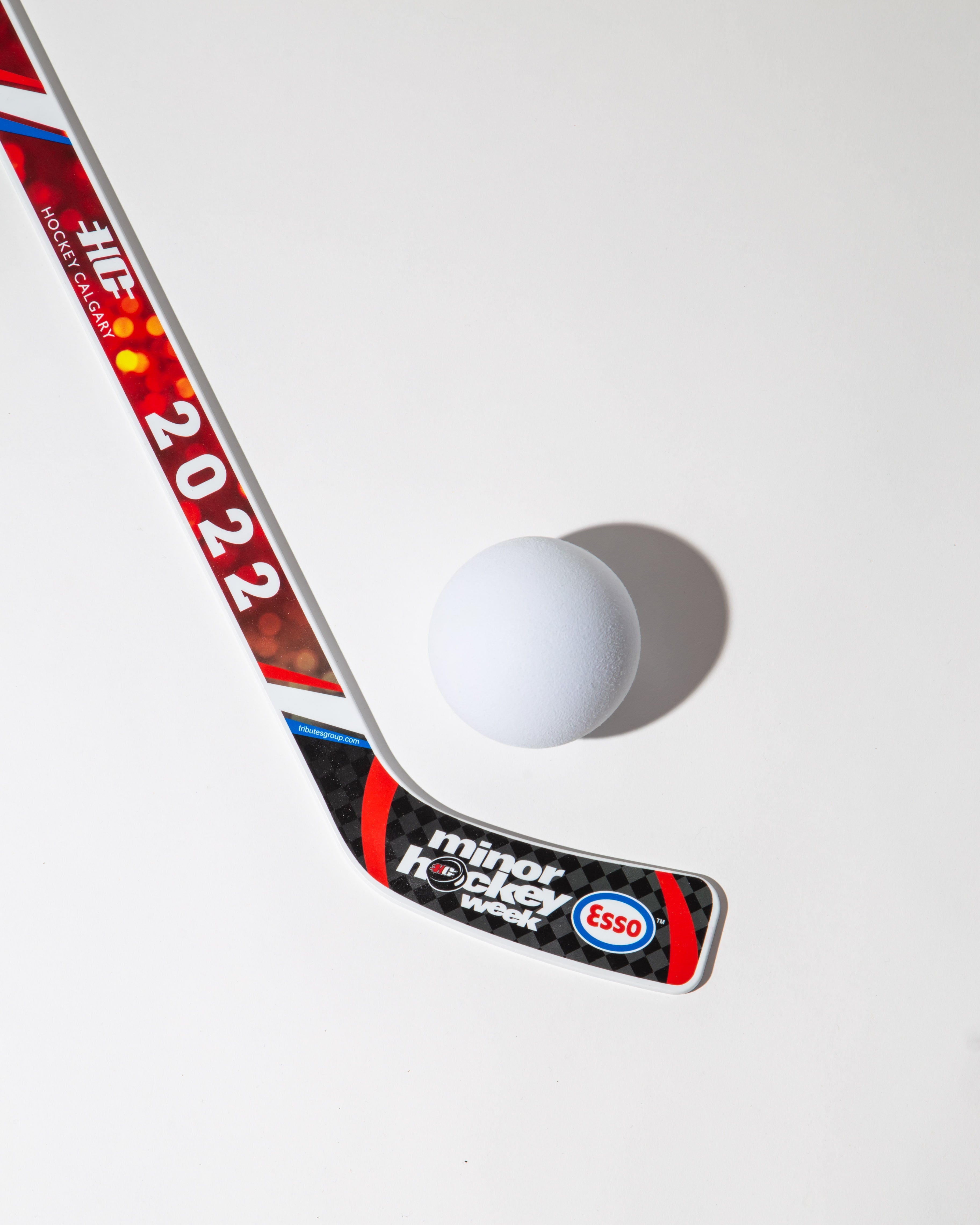 Hockey stick with '2022' and 'minor hockey week' branding next to a white ball on a white background.
