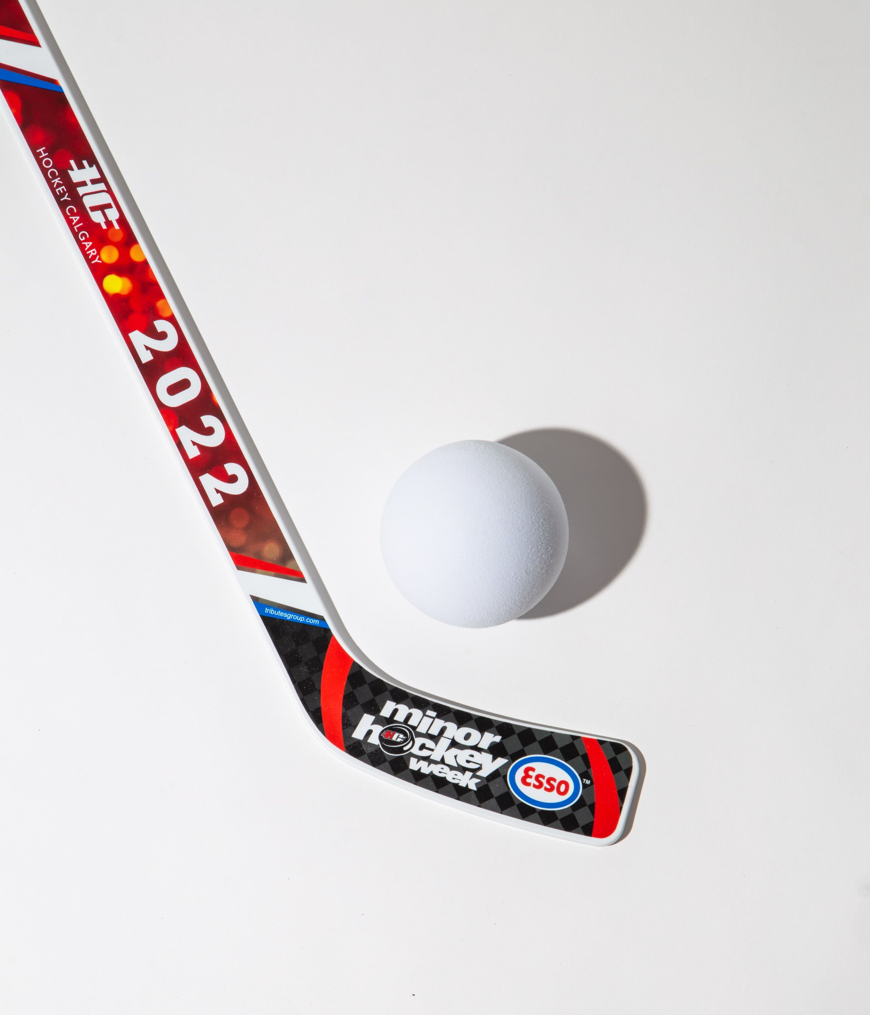 Hockey stick with '2022' and 'minor hockey week' branding next to a white ball on a white background.