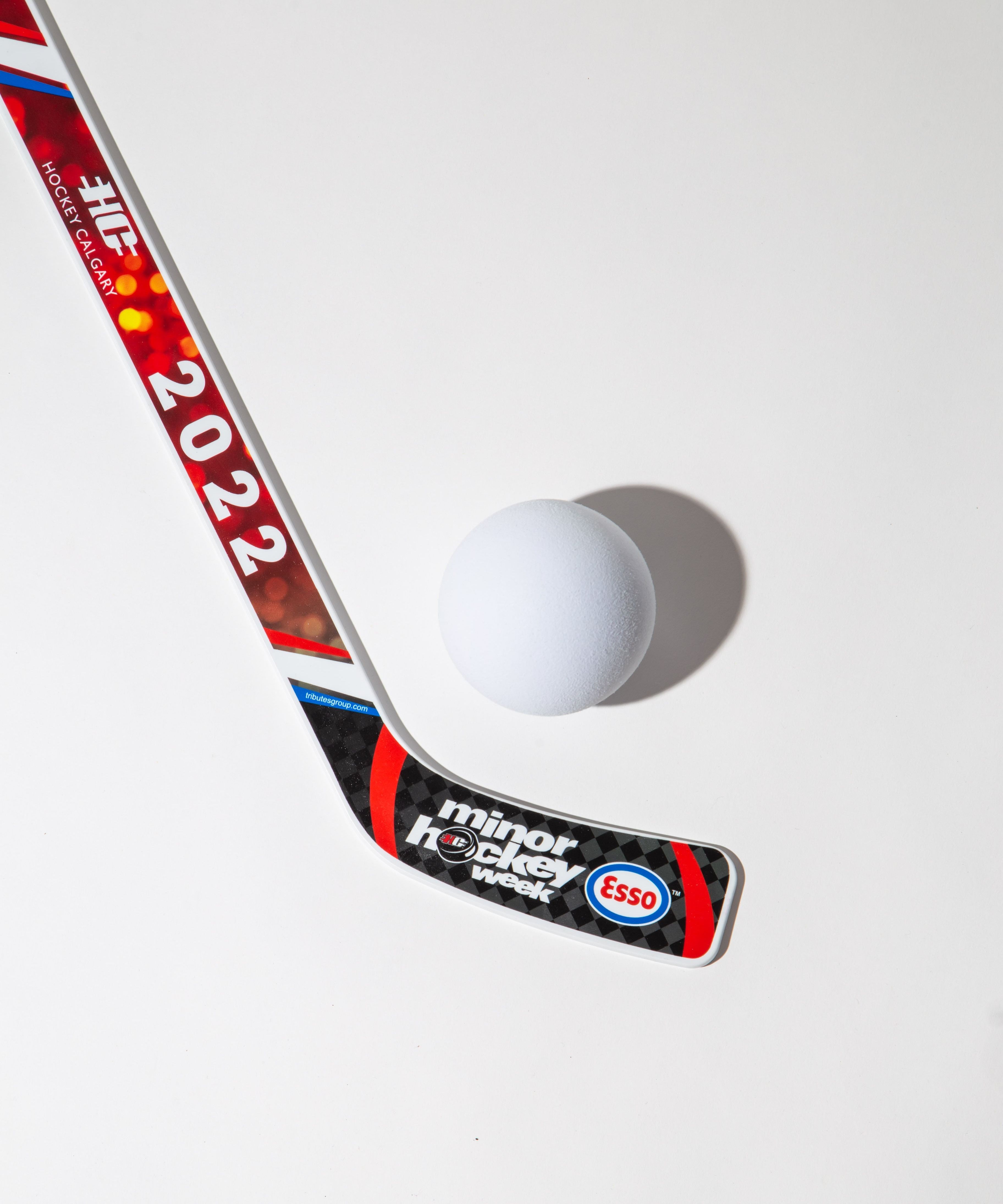 Hockey stick with '2022' and 'minor hockey week' branding next to a white ball on a white background.