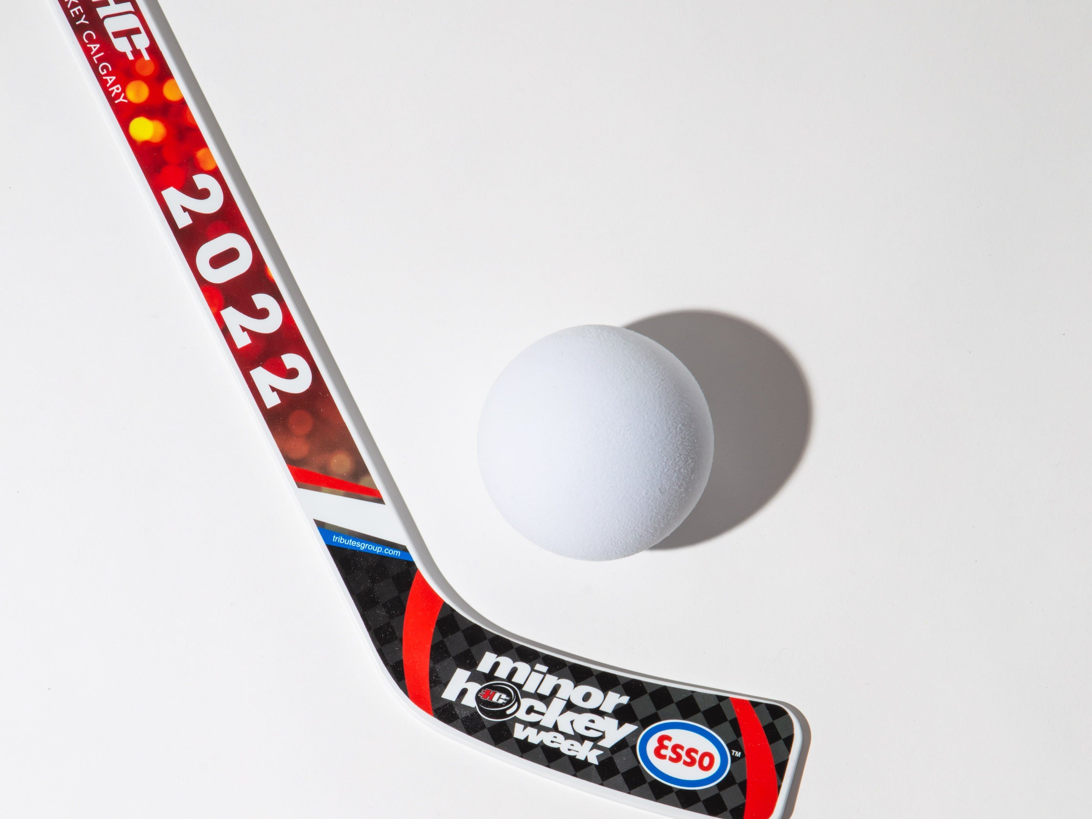 Hockey stick with '2022' and 'minor hockey week' branding next to a white ball on a white background.
