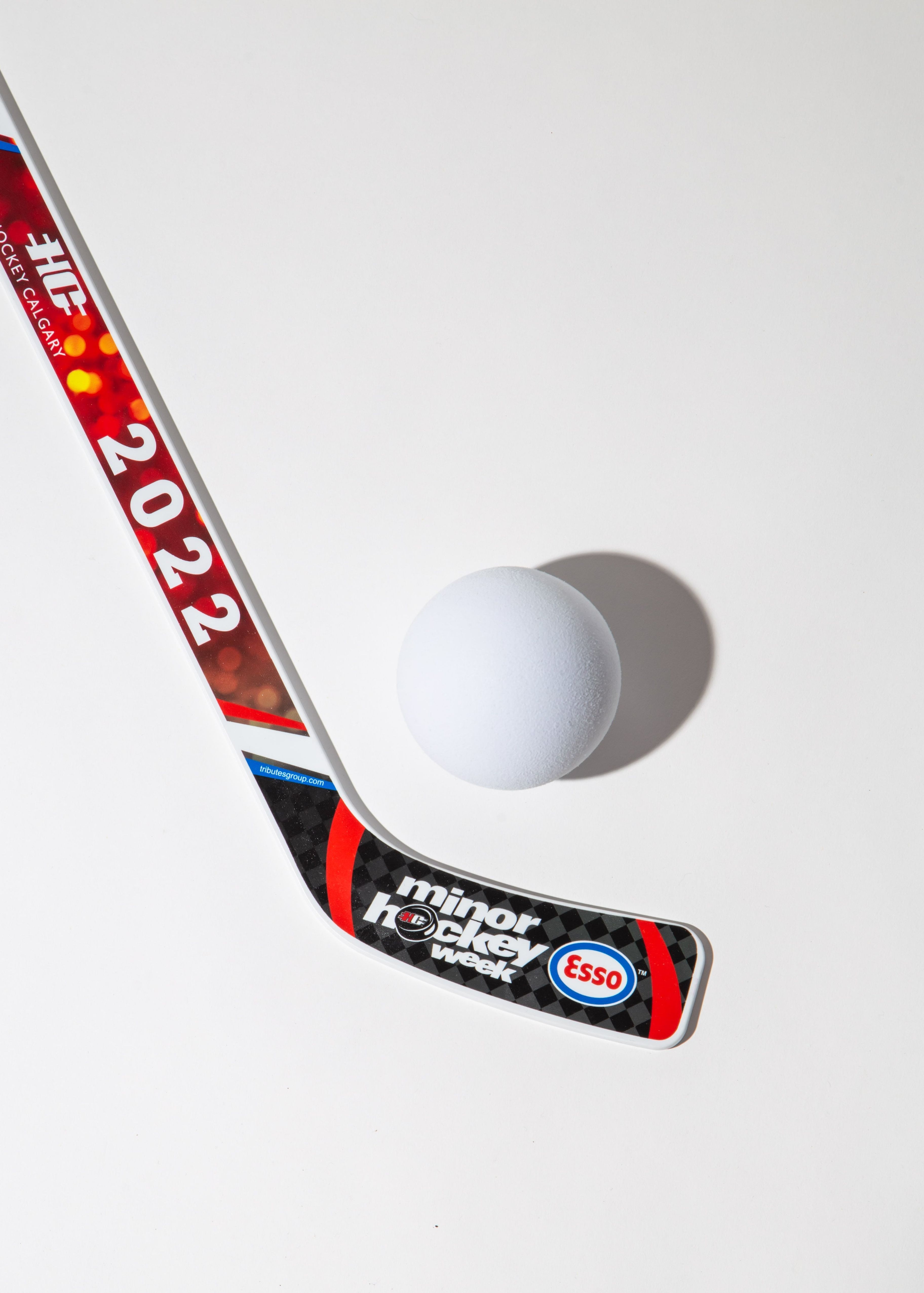 Hockey stick with '2022' and 'minor hockey week' branding next to a white ball on a white background.