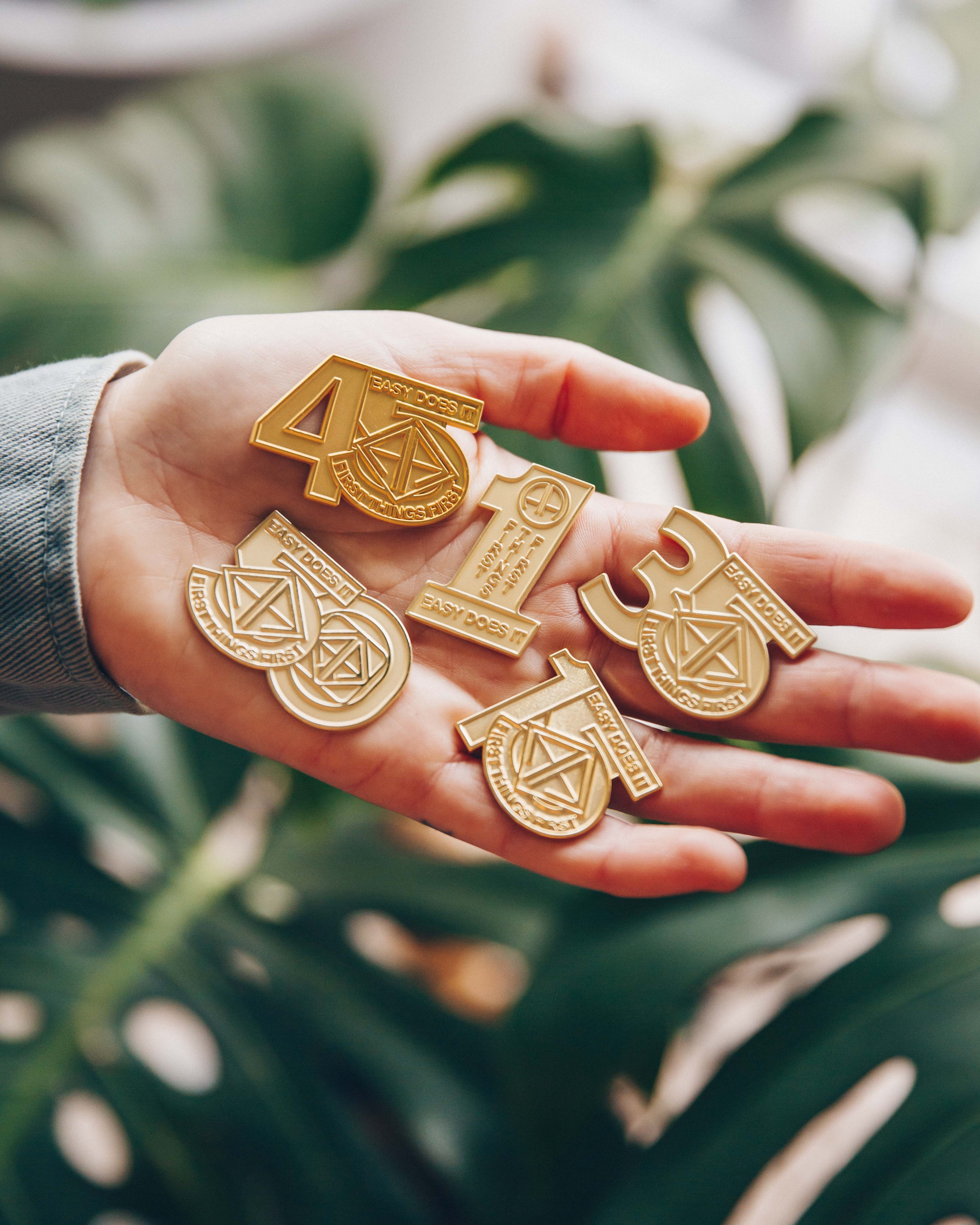 Hand holding gold AA medallions with various numbers and symbols, against a leafy background.