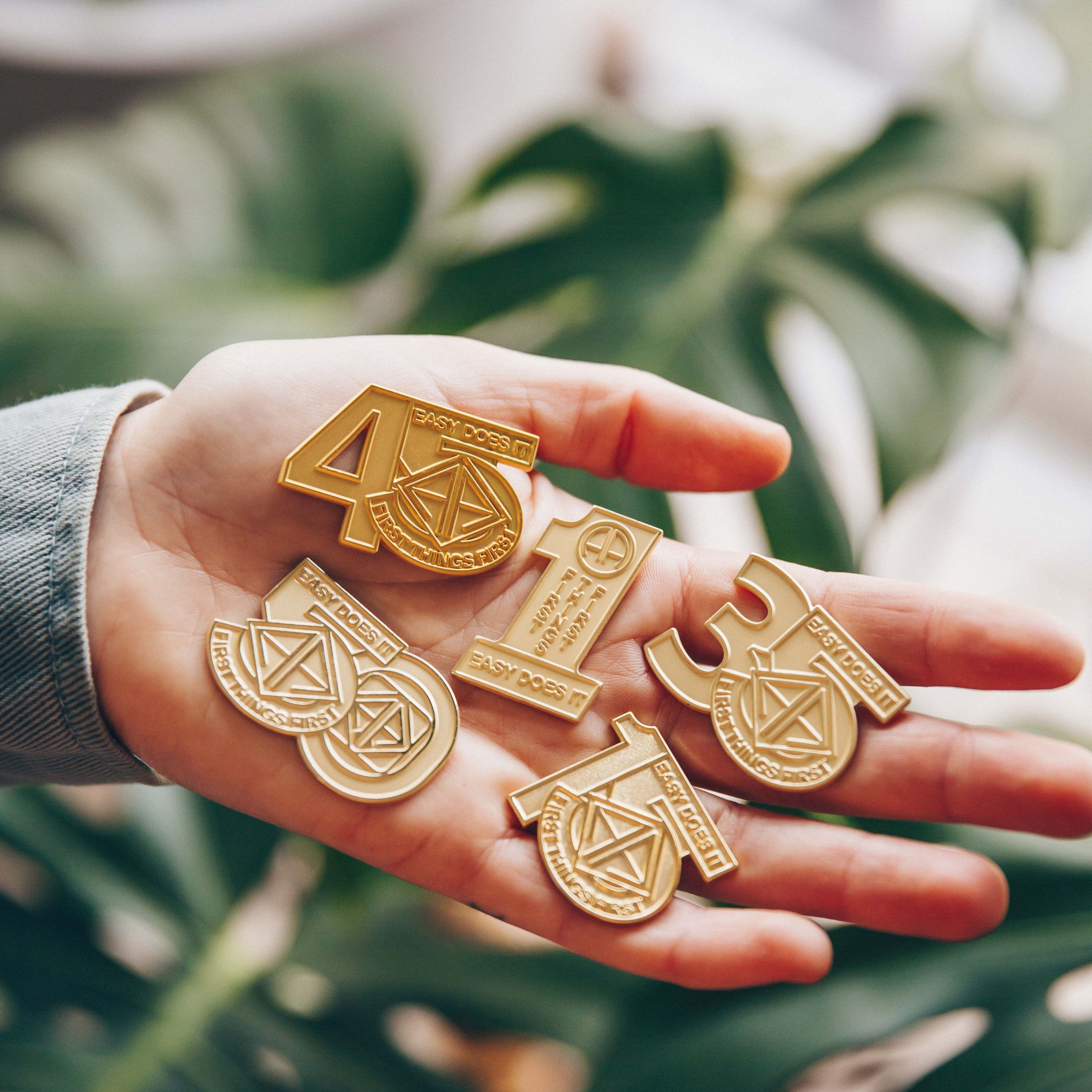 Hand holding gold AA medallions with various numbers and symbols, against a leafy background.
