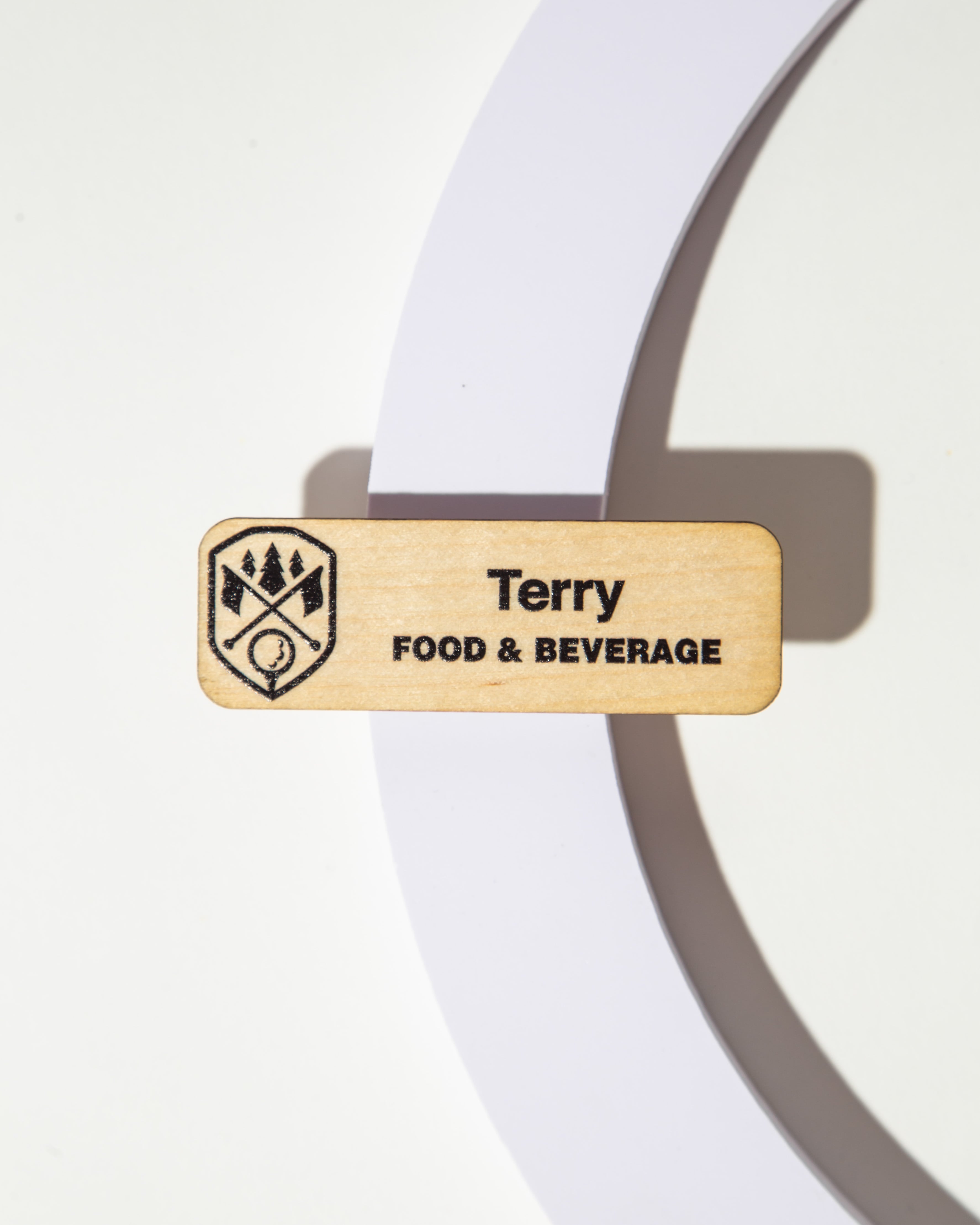 Wooden name tag with 'Terry' and 'Food & Beverage' engraved, featuring a logo, on a white background.