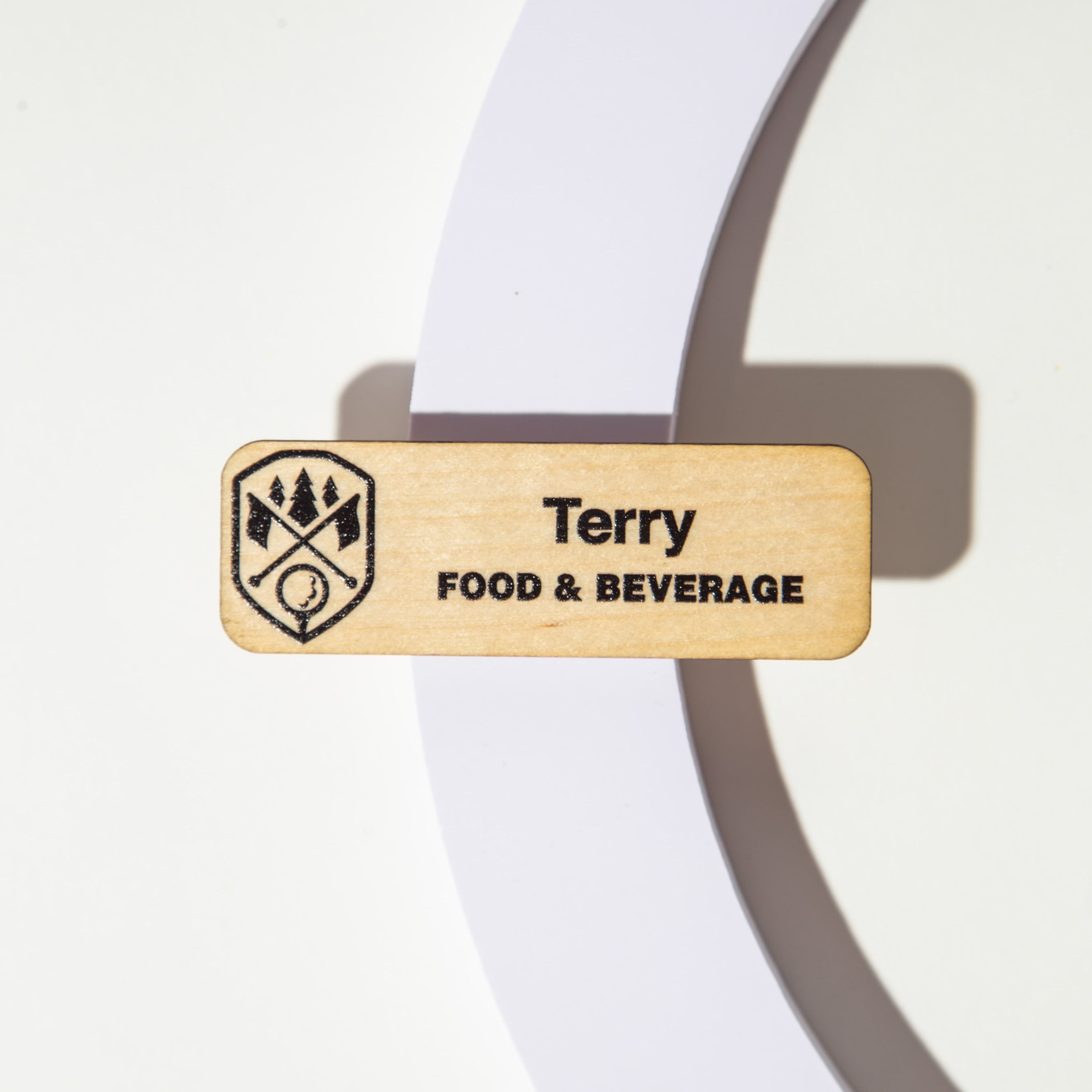Wooden name tag with 'Terry' and 'Food & Beverage' engraved, featuring a logo, on a white background.
