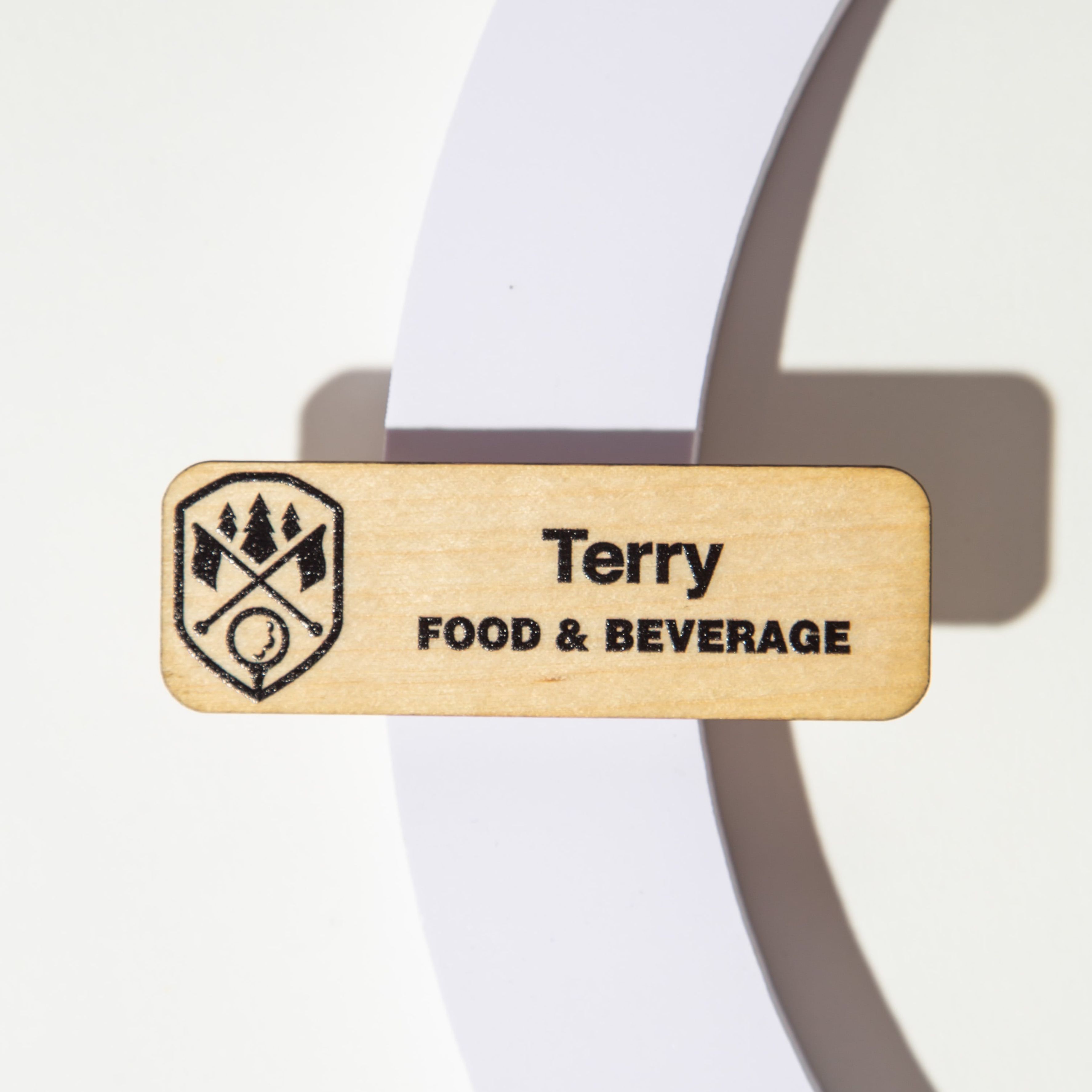 Wooden name tag with 'Terry' and 'Food & Beverage' engraved, featuring a logo, on a white background.