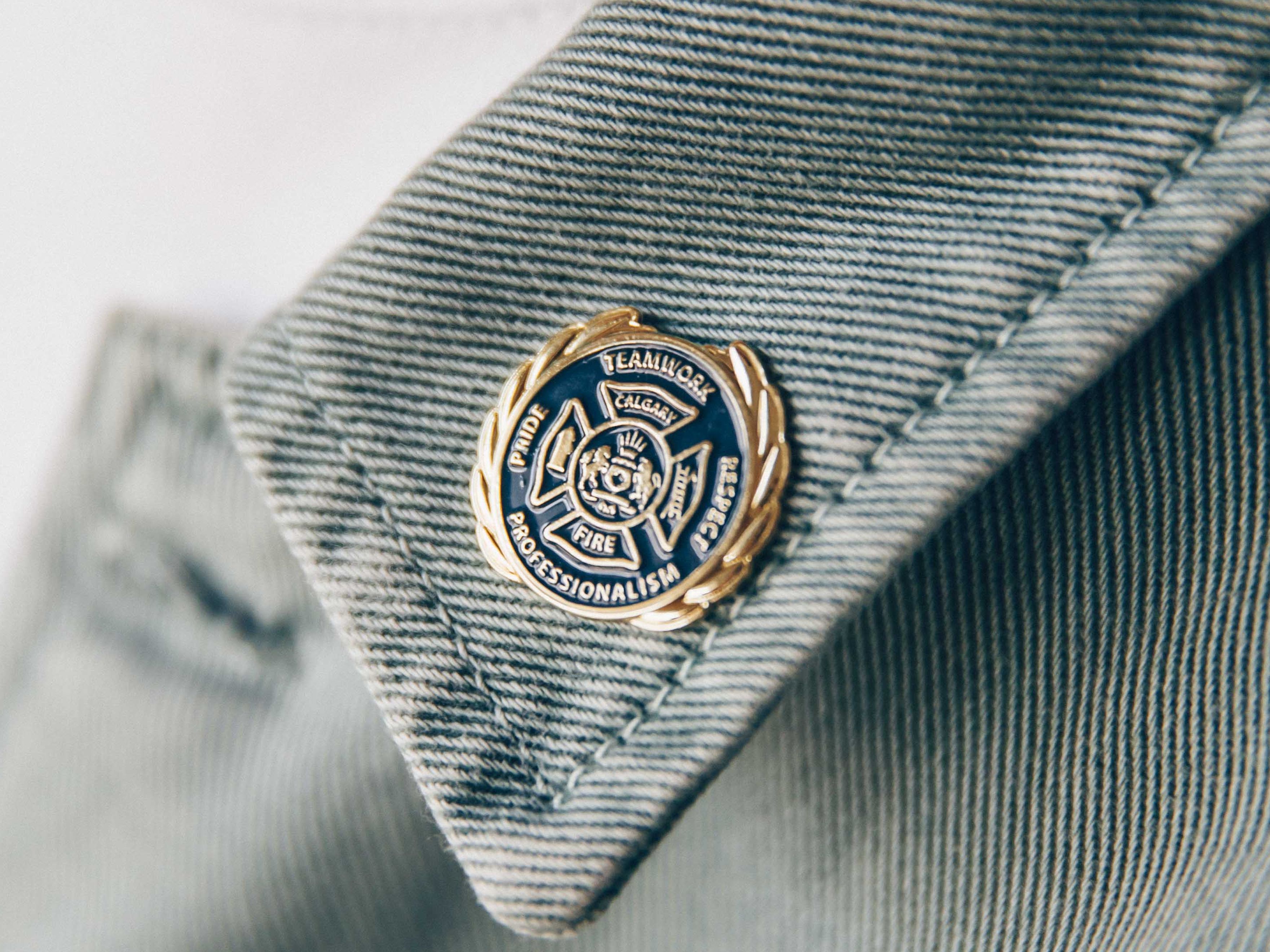 Close-up of a circular enamel pin on grey denim jacket collar, with white t-shirt visible underneath.