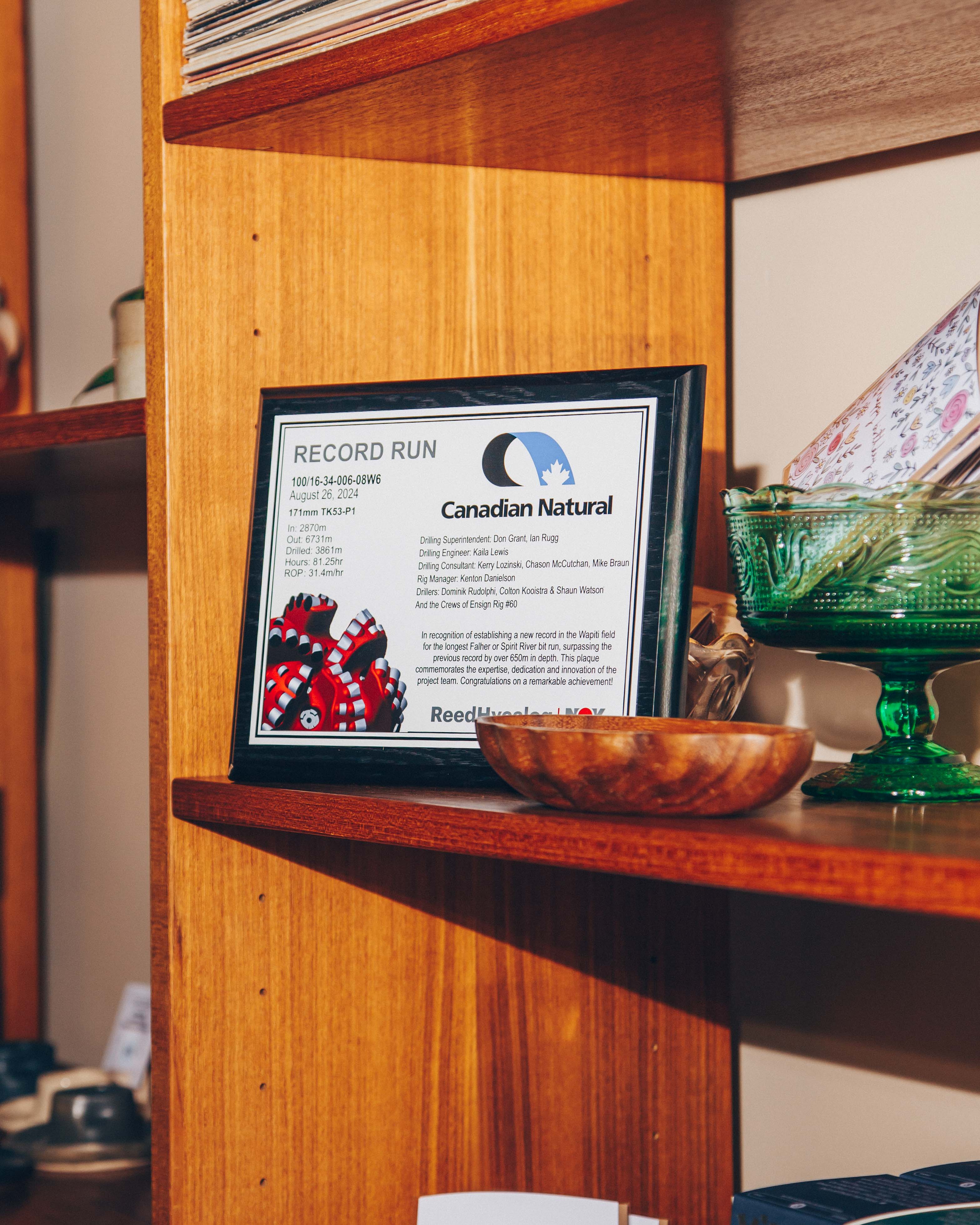 Plaque on a wooden shelf commemorating a record run by Canadian Natural, surrounded by decorative items.