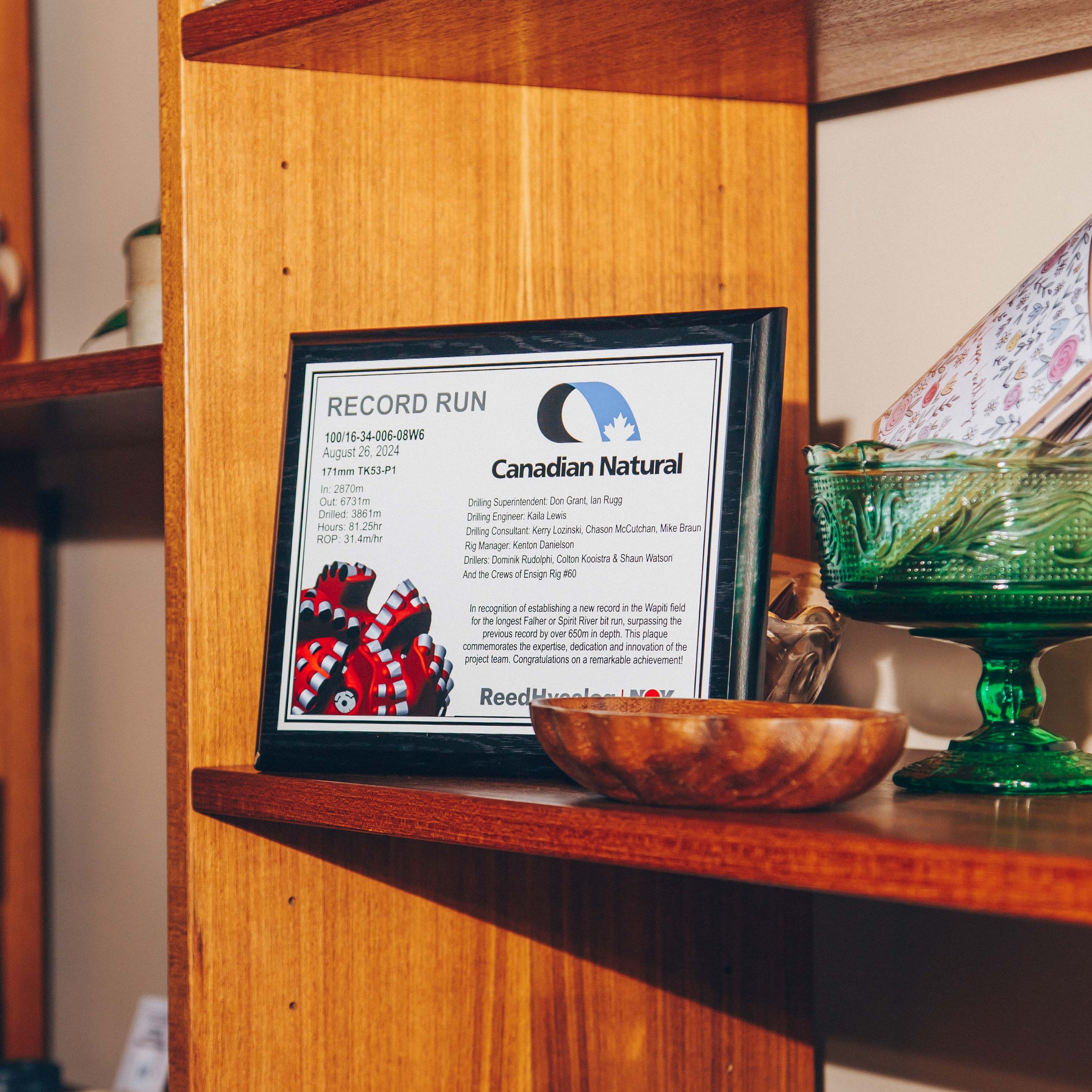 Plaque on a wooden shelf commemorating a record run by Canadian Natural, surrounded by decorative items.