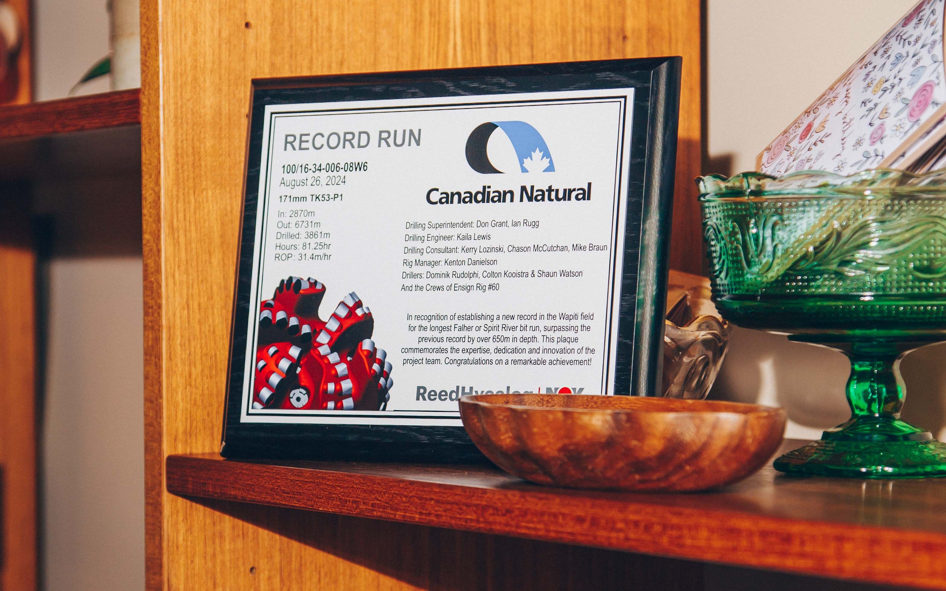 Plaque on a wooden shelf commemorating a record run by Canadian Natural, surrounded by decorative items.