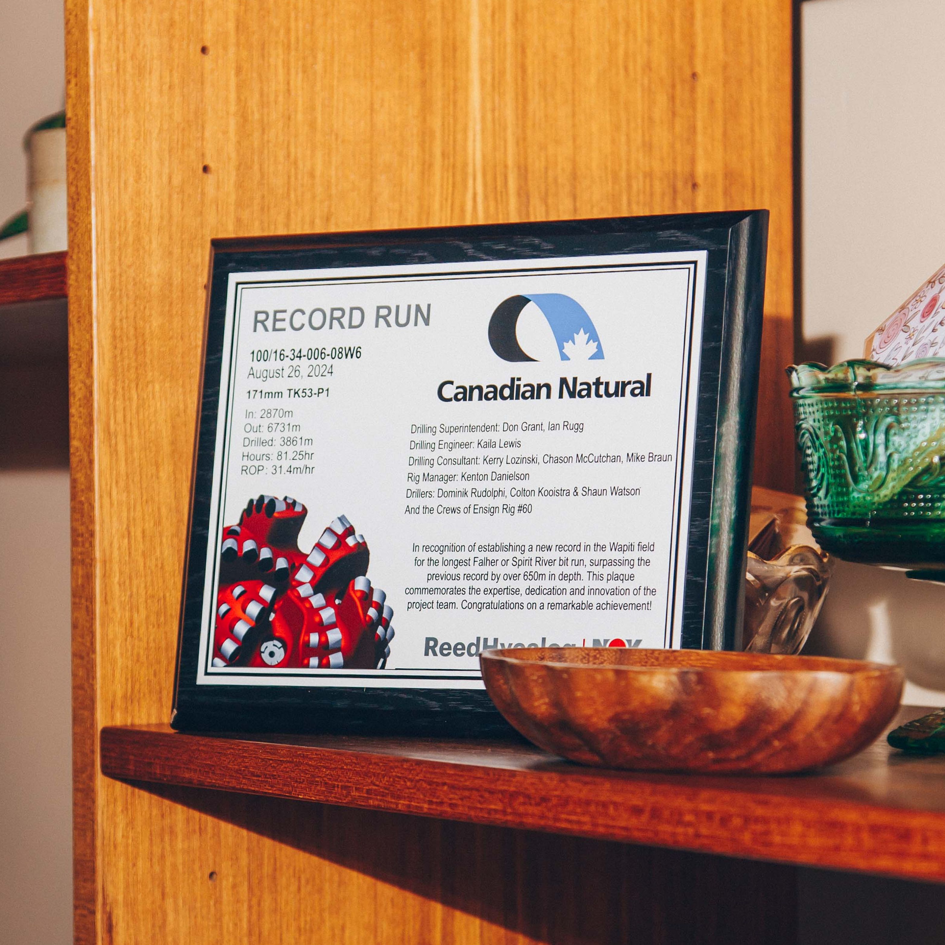 Plaque on a wooden shelf commemorating a record run by Canadian Natural, surrounded by decorative items.