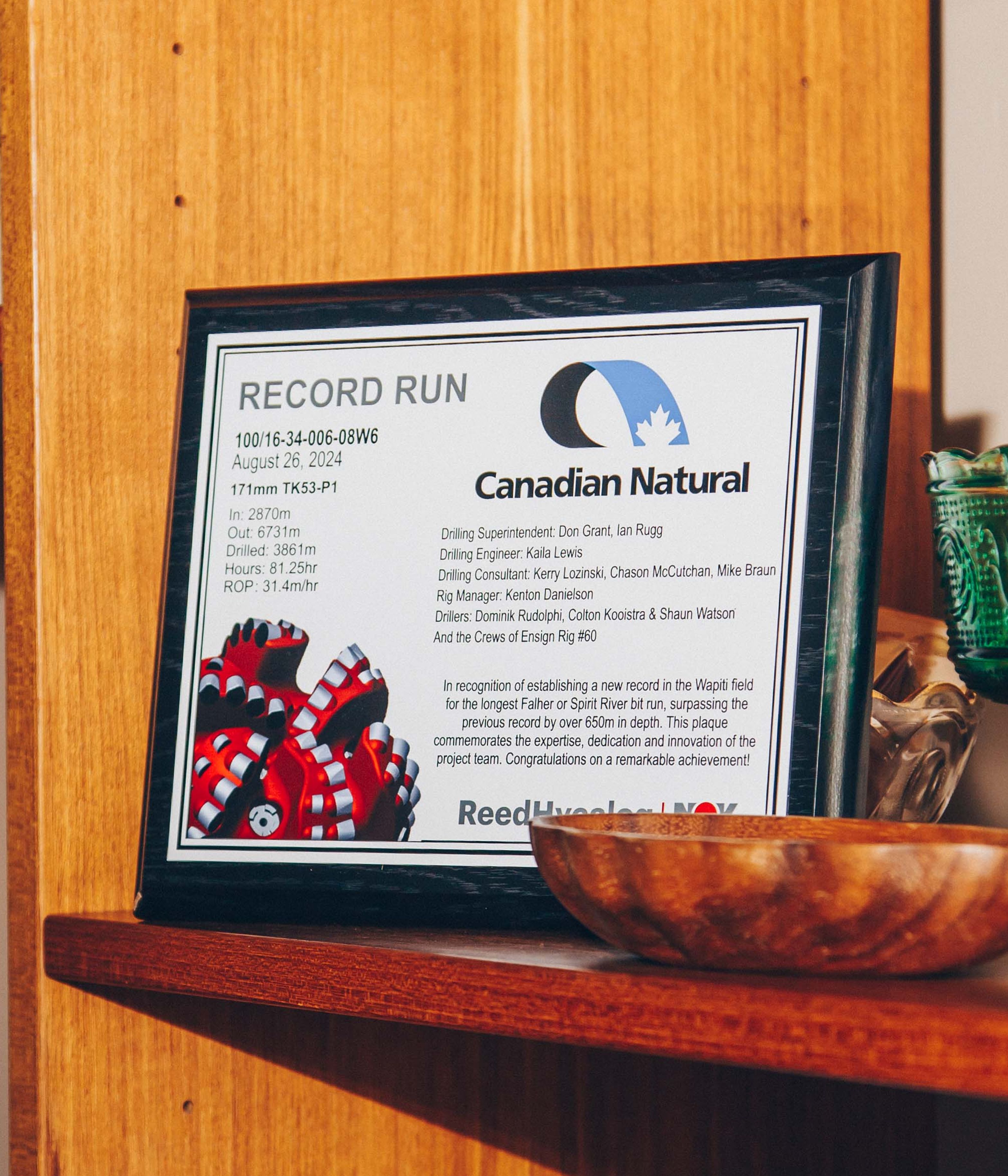 Plaque on a wooden shelf commemorating a record run by Canadian Natural, surrounded by decorative items.