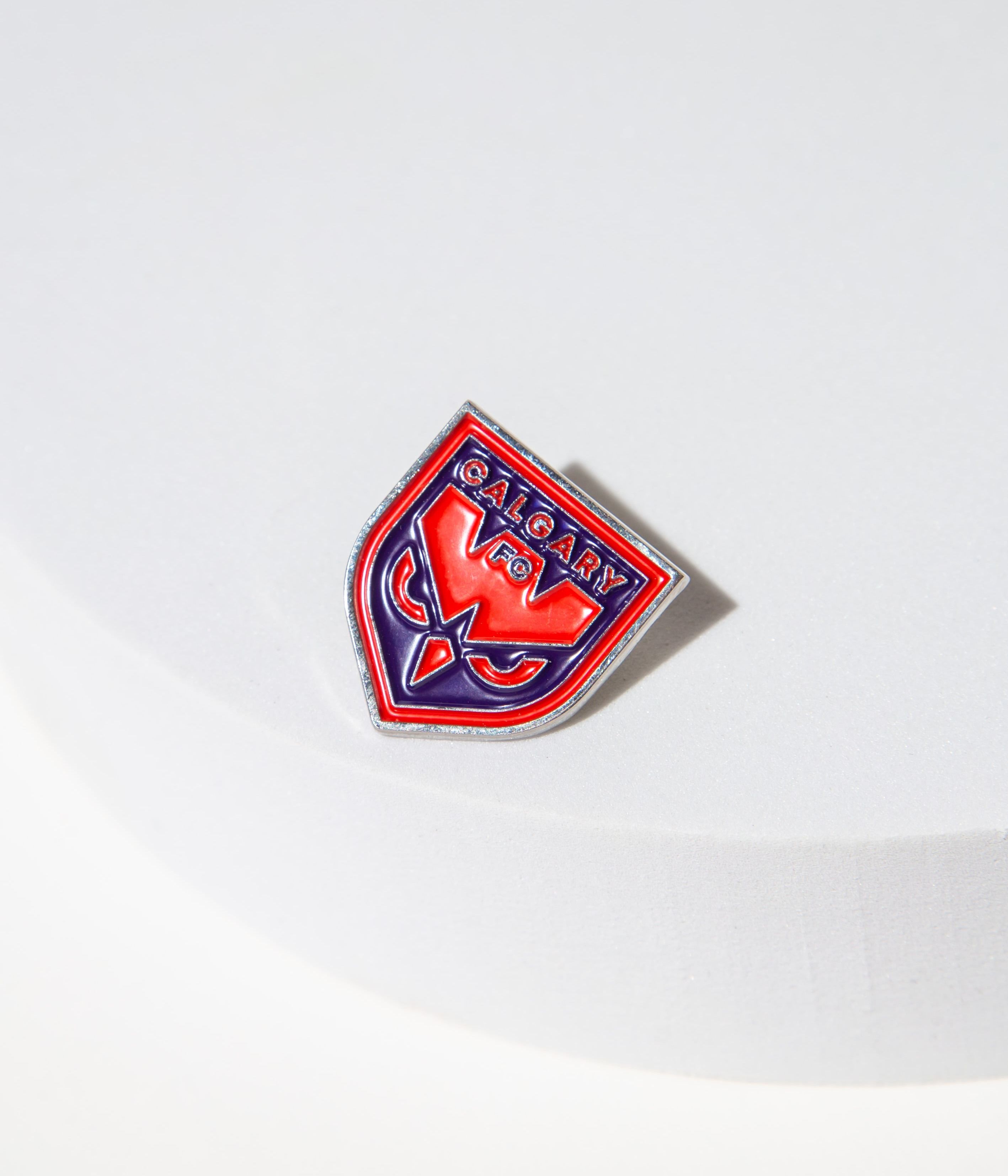 Red and blue Calgary FC enamel pin on a white surface.