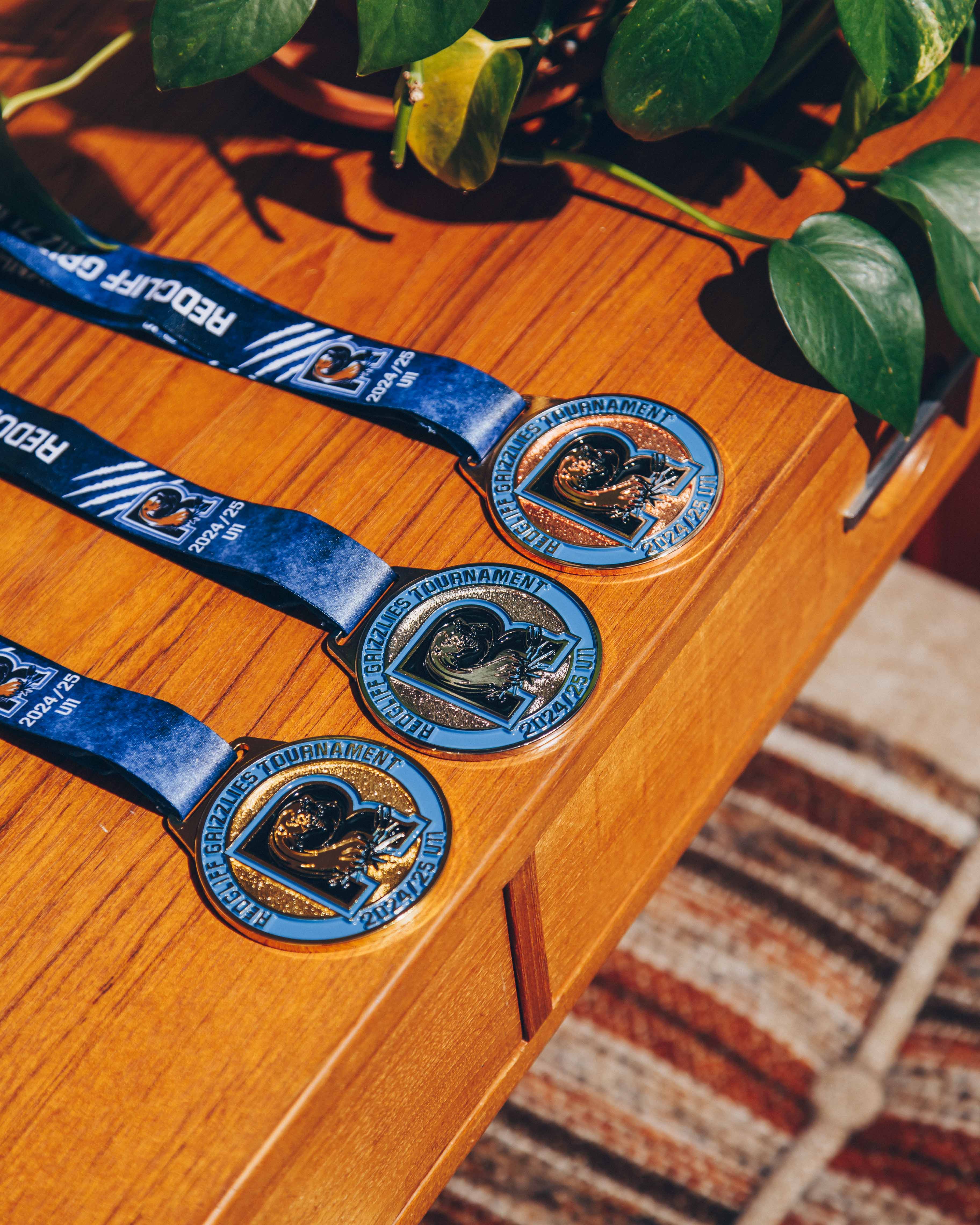 Three custom Red Bluff Grapplers Tournament 2024-25 medals displayed on a wooden table, crafted for youth wrestling events.