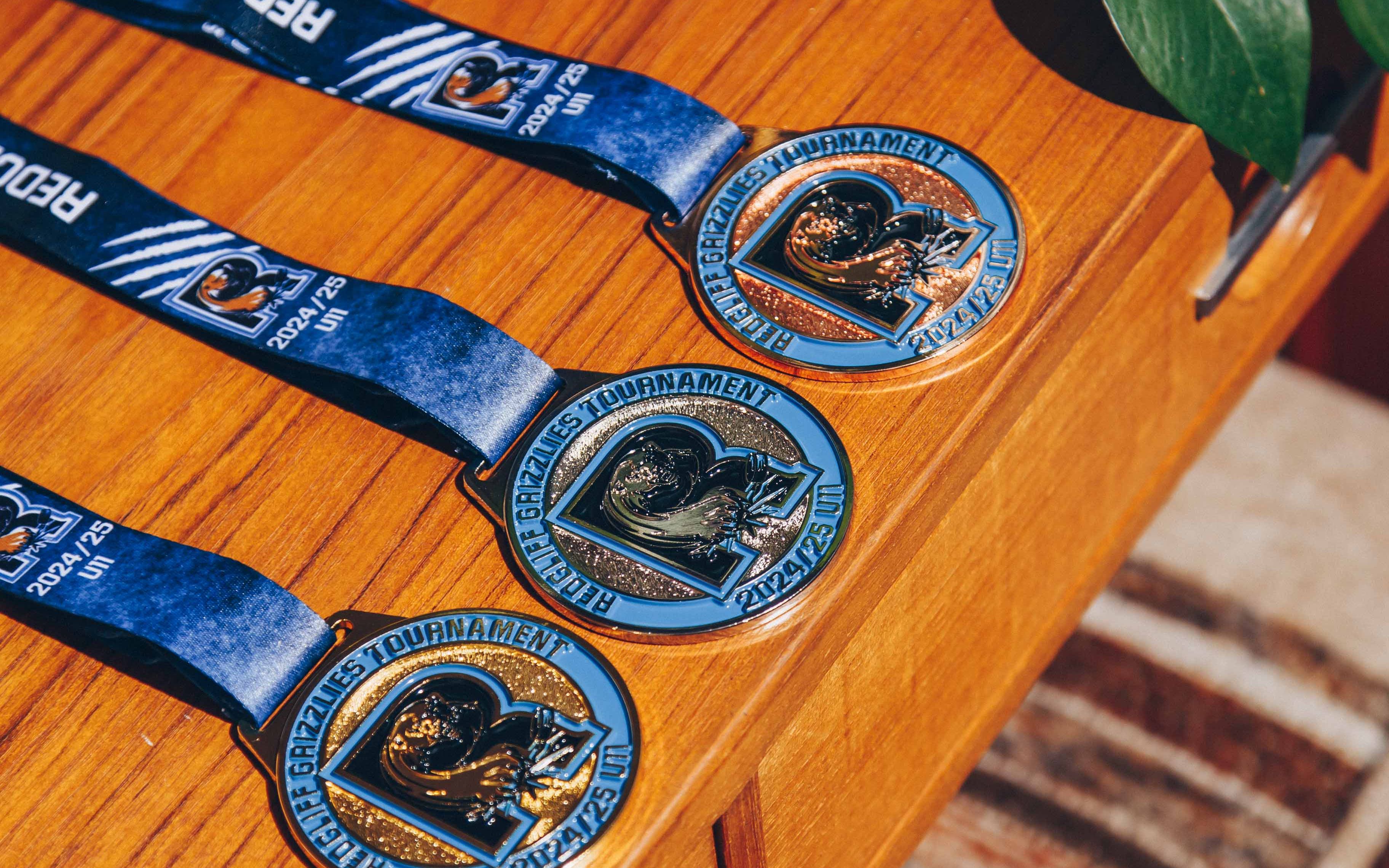 Three custom Red Bluff Grapplers Tournament 2024-25 medals displayed on a wooden table, crafted for youth wrestling events.