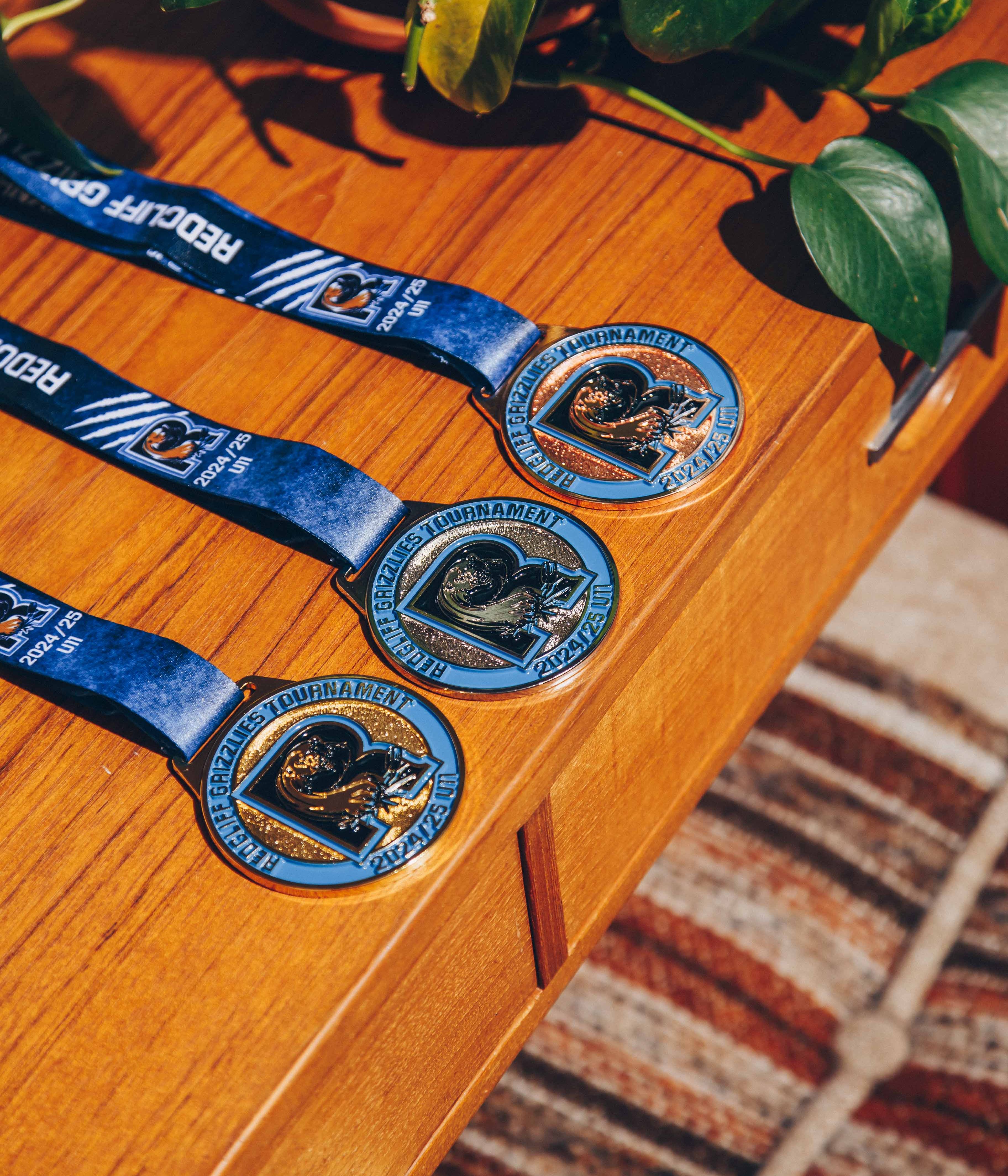 Three custom Red Bluff Grapplers Tournament 2024-25 medals displayed on a wooden table, crafted for youth wrestling events.
