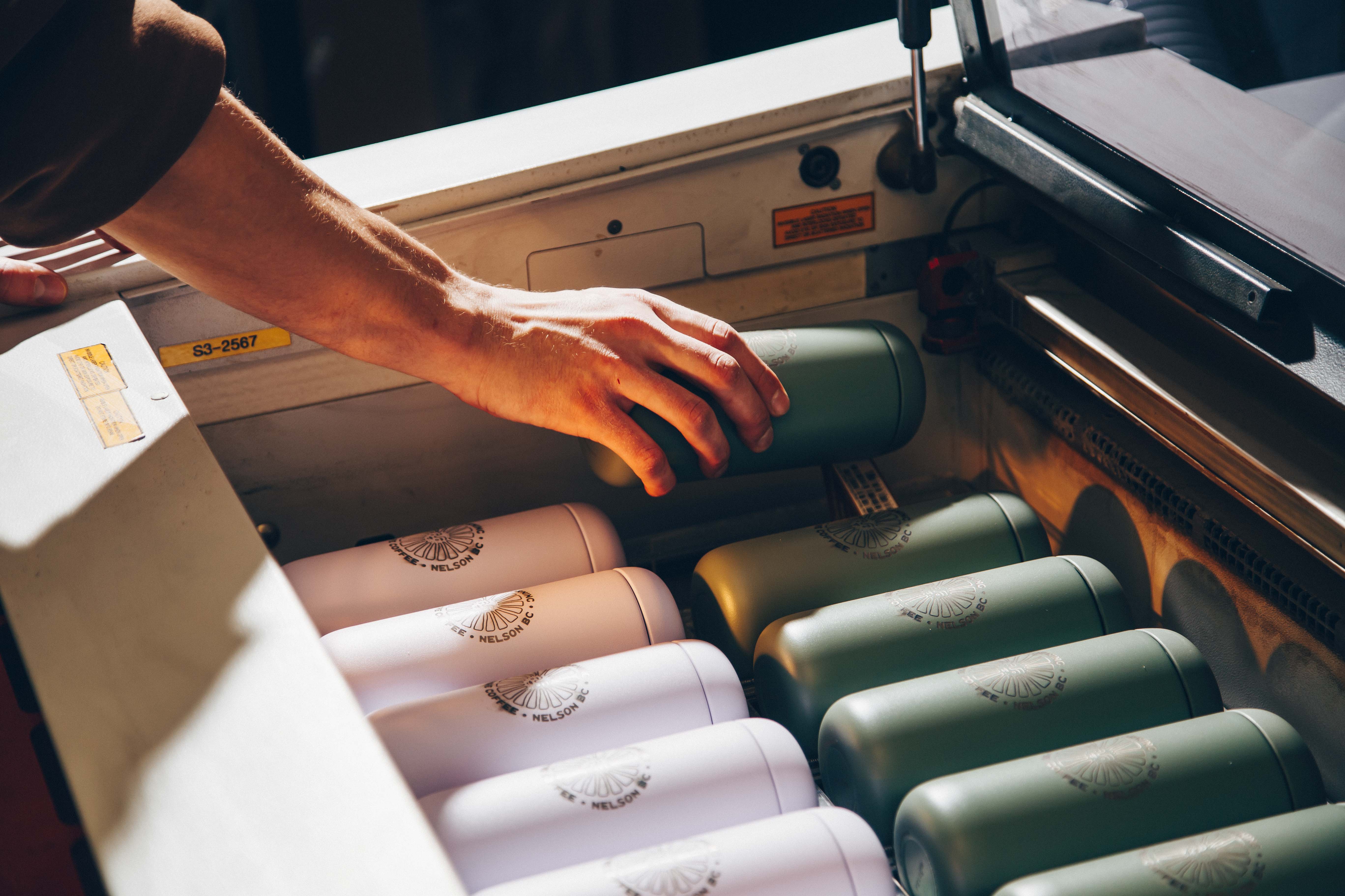 Hands reaching for reusable water bottles arranged in rows of pink and green, each marked with the Nelson brand logo.