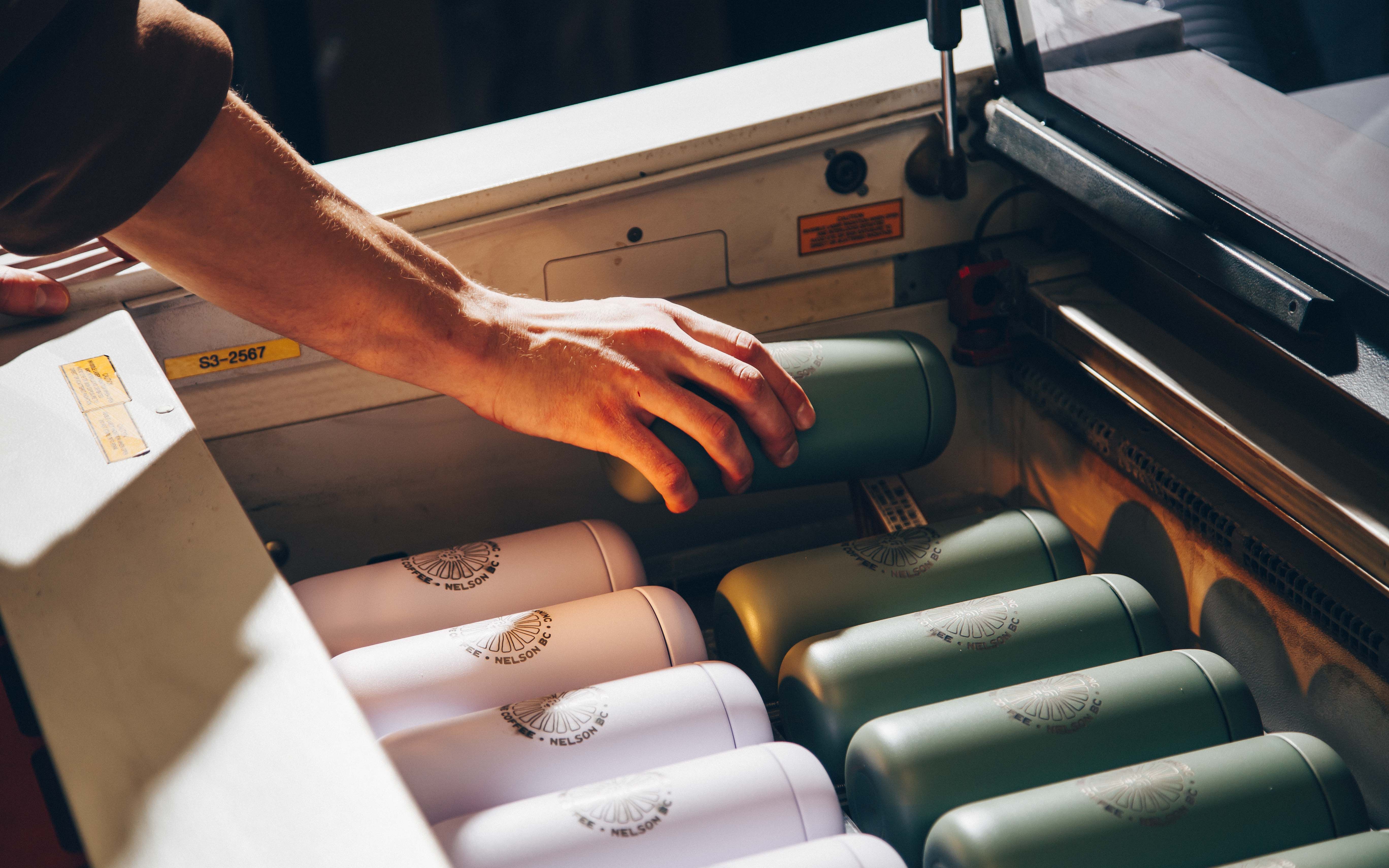 Hands reaching for reusable water bottles arranged in rows of pink and green, each marked with the Nelson brand logo.