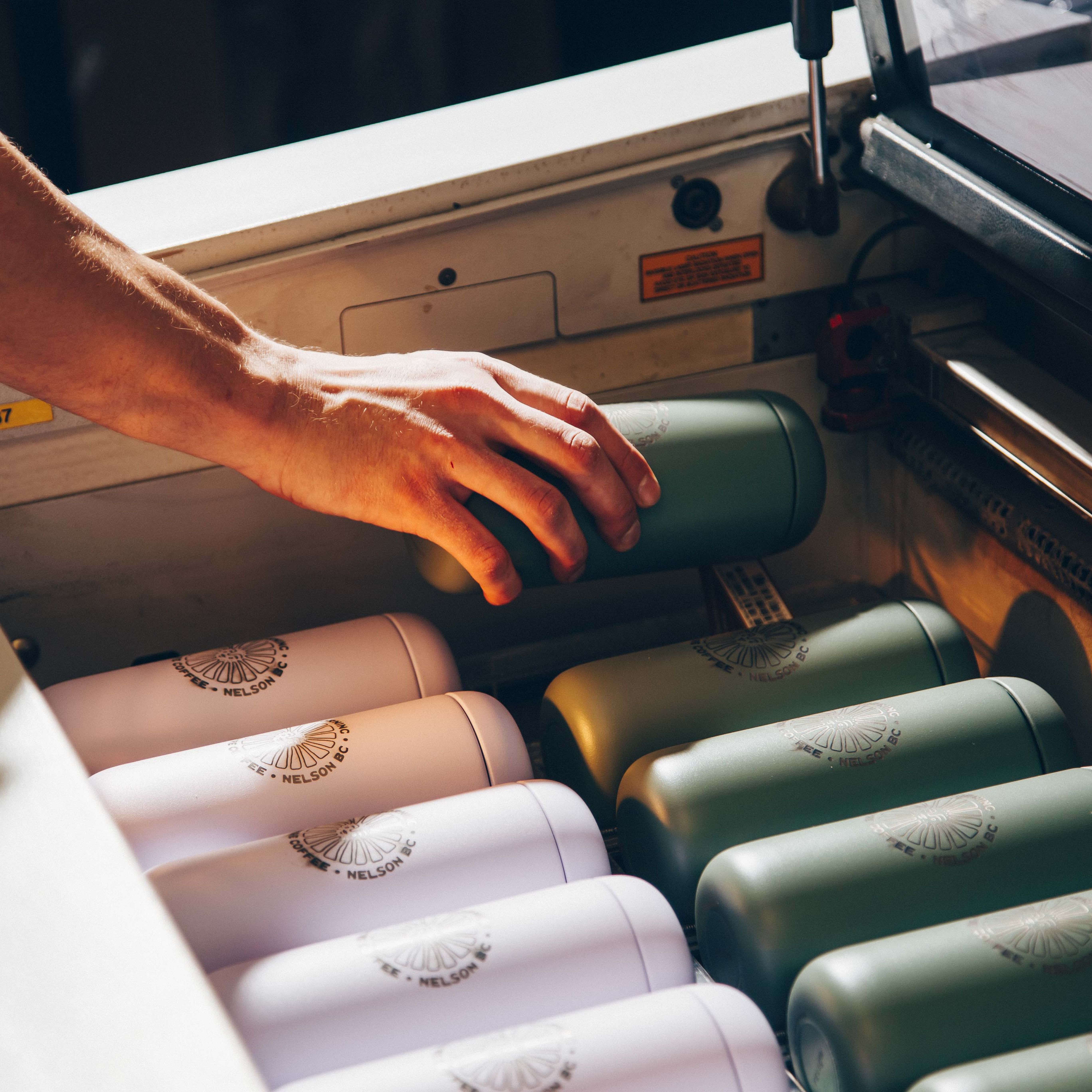 Hands reaching for reusable water bottles arranged in rows of pink and green, each marked with the Nelson brand logo.
