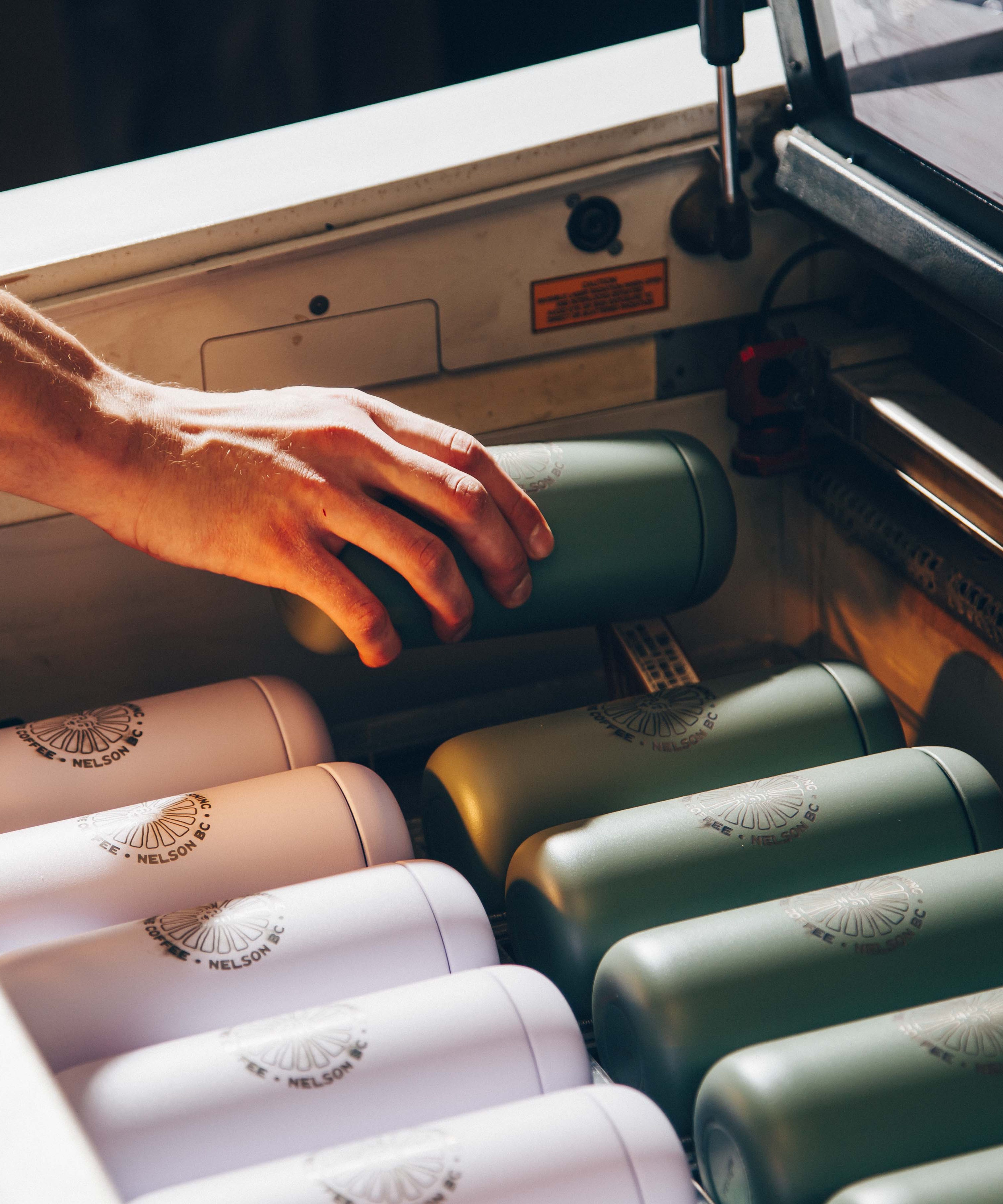 Hands reaching for reusable water bottles arranged in rows of pink and green, each marked with the Nelson brand logo.