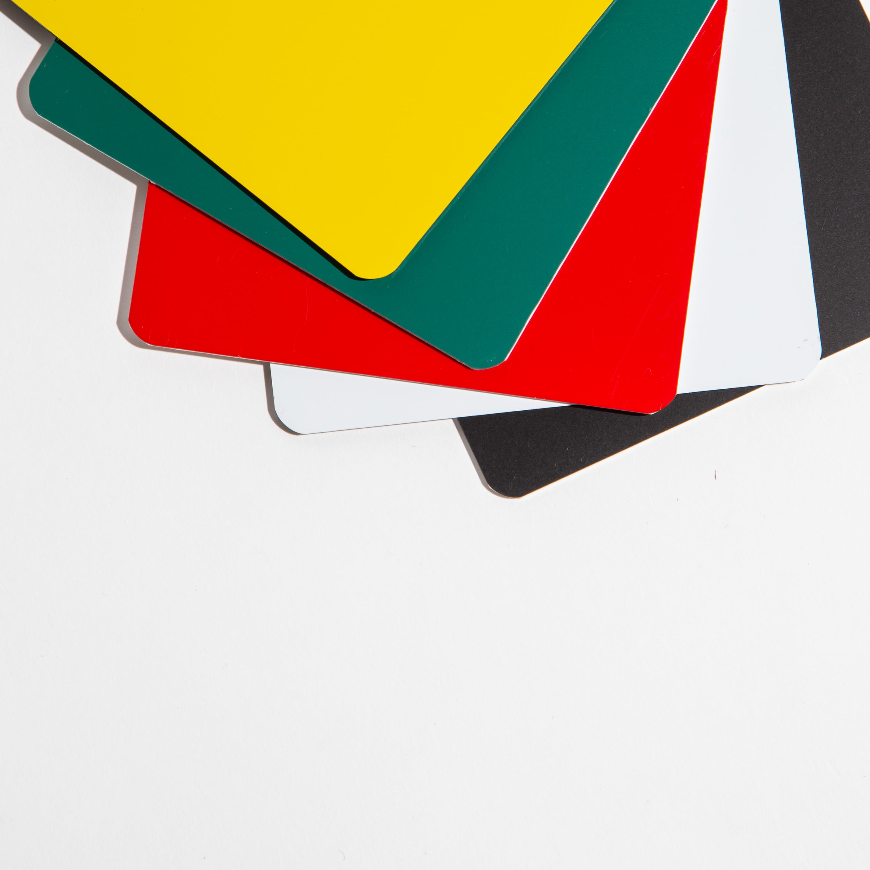 Stack of colorful plastic sheets in yellow, green, red, white, and black on a white background.