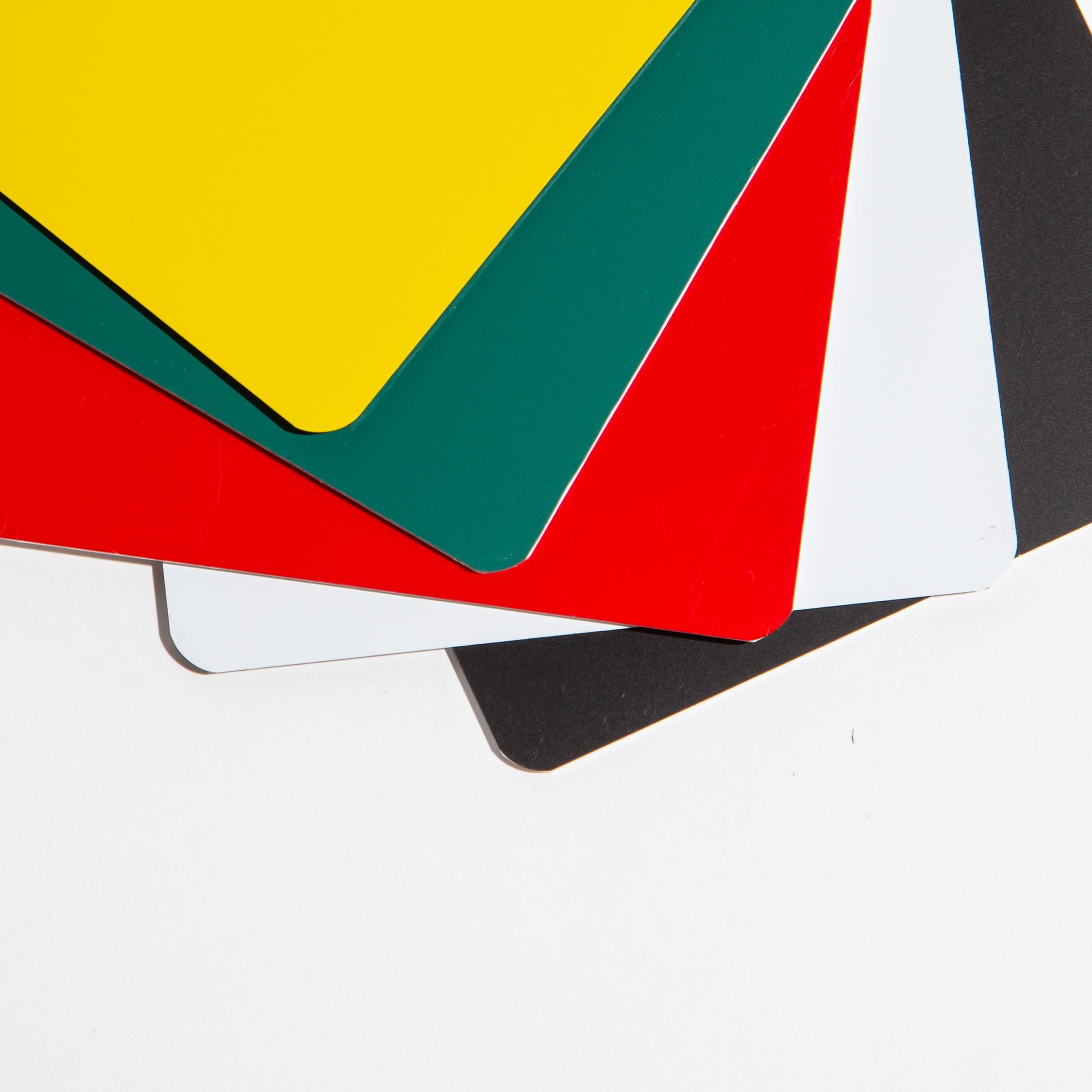 Stack of colorful plastic sheets in yellow, green, red, white, and black on a white background.