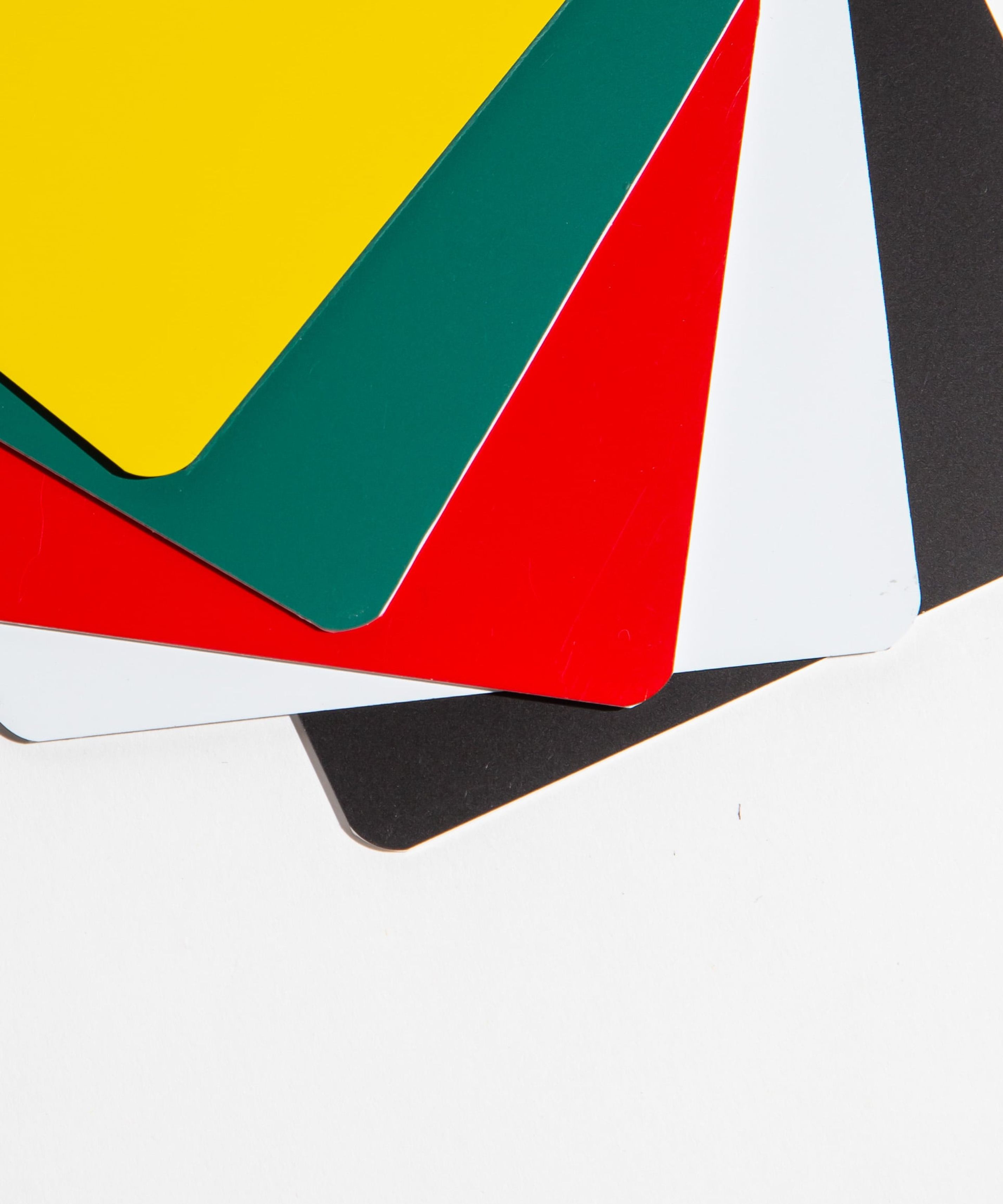 Stack of colorful plastic sheets in yellow, green, red, white, and black on a white background.