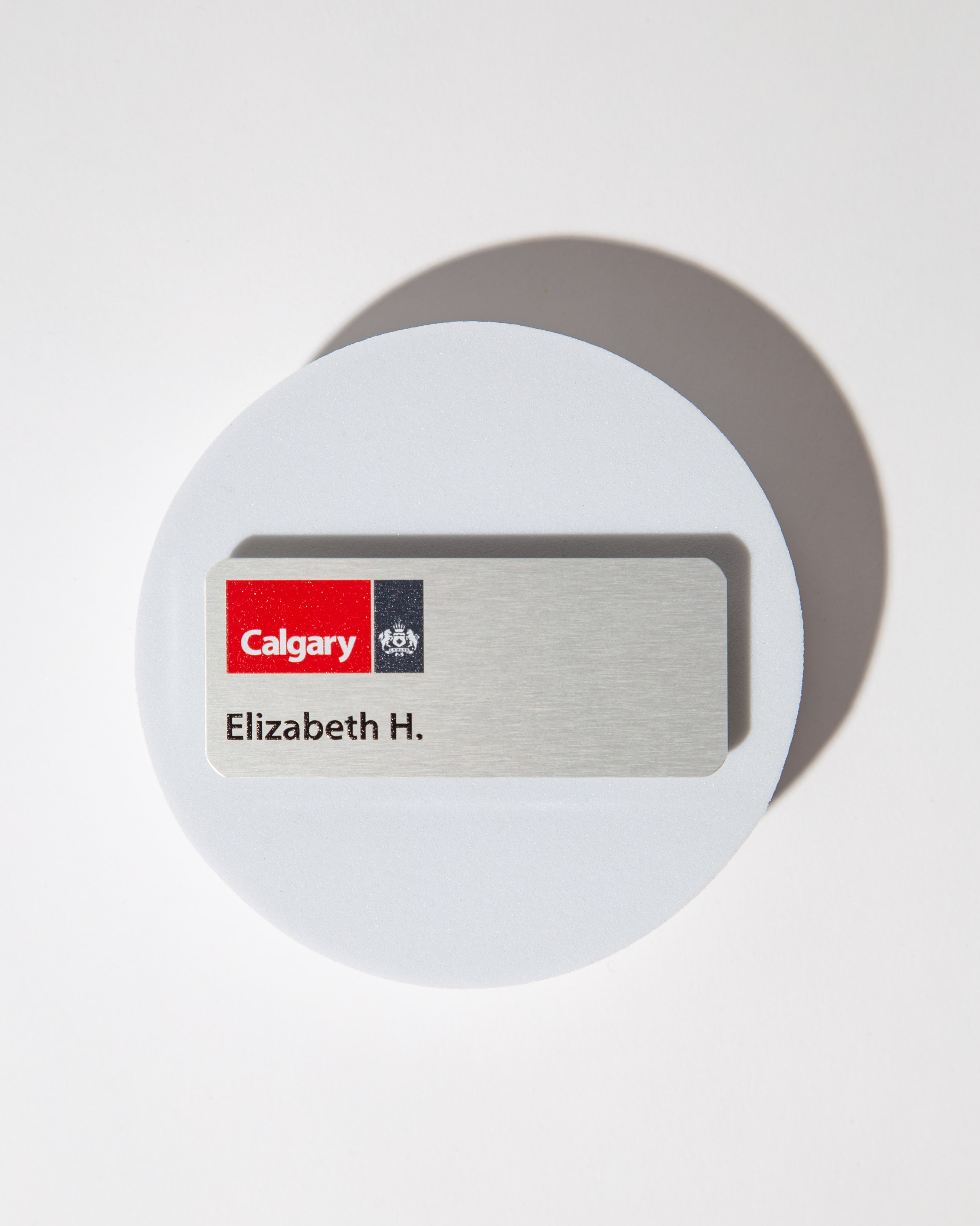 Name tag with 'Calgary' logo and 'Elizabeth H.' text on a silver aluminum background.
