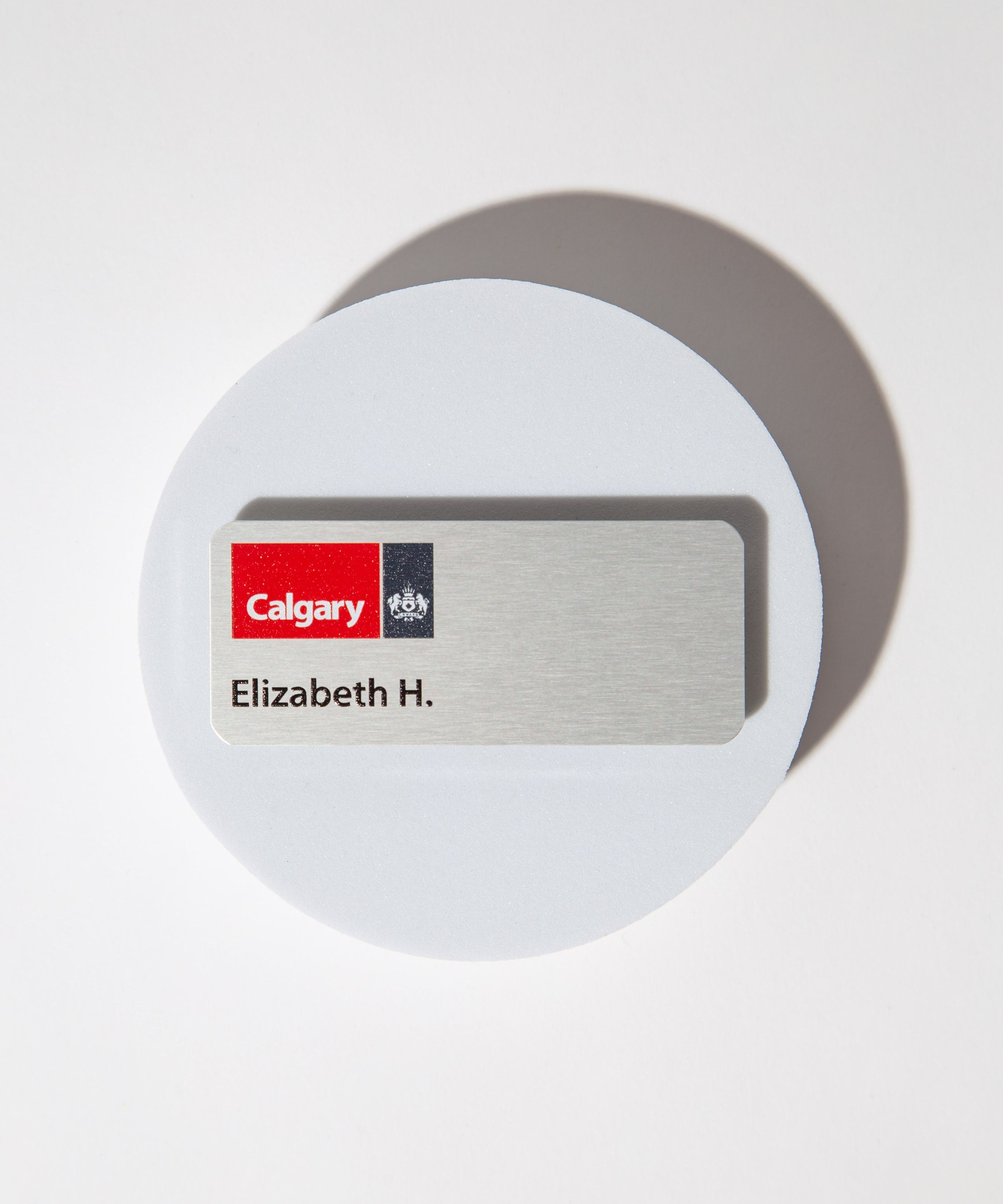 Name tag with 'Calgary' logo and 'Elizabeth H.' text on a silver aluminum background.