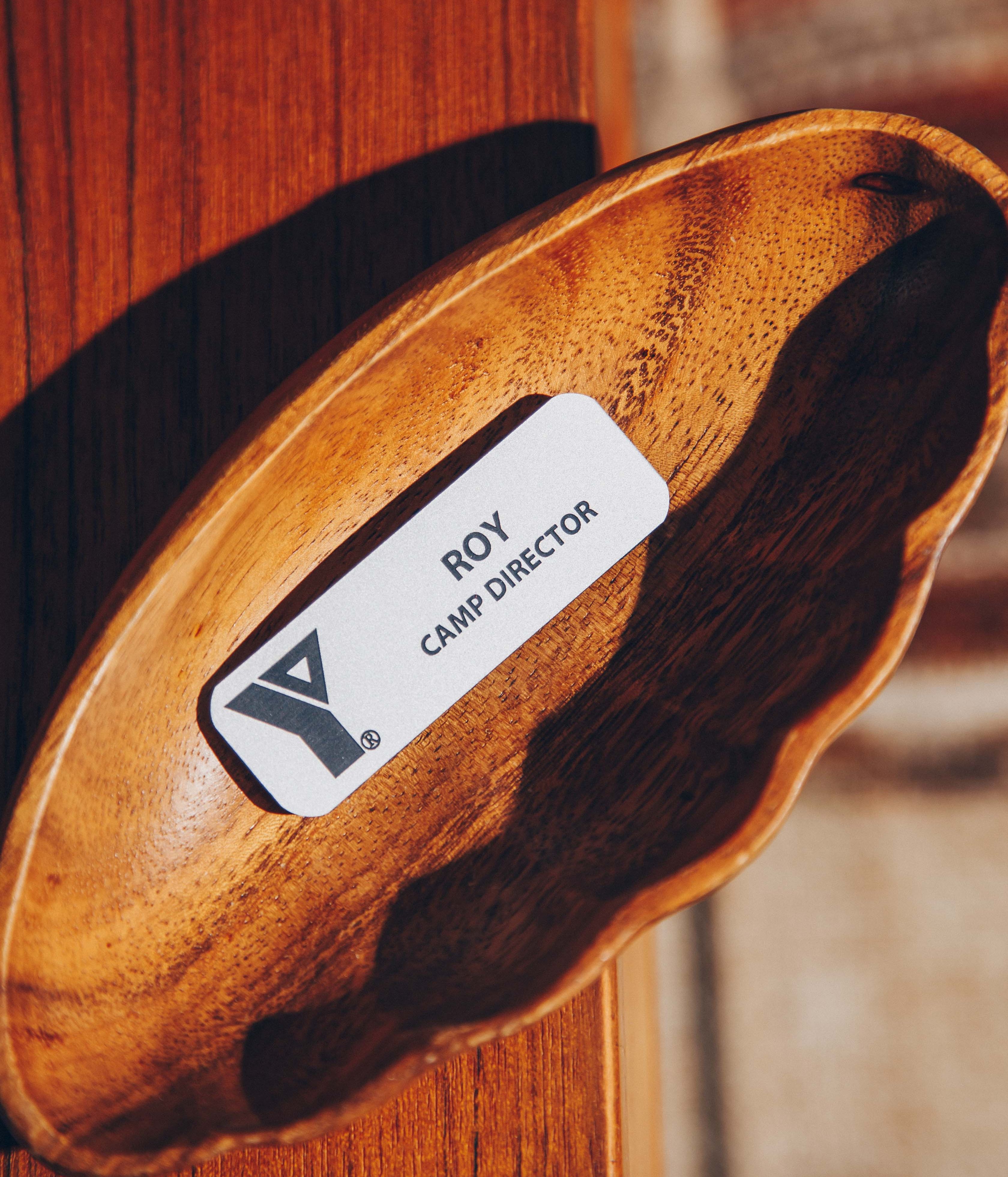Wooden bowl holding a name tag labeled 'Camp Director' on a wooden surface.
