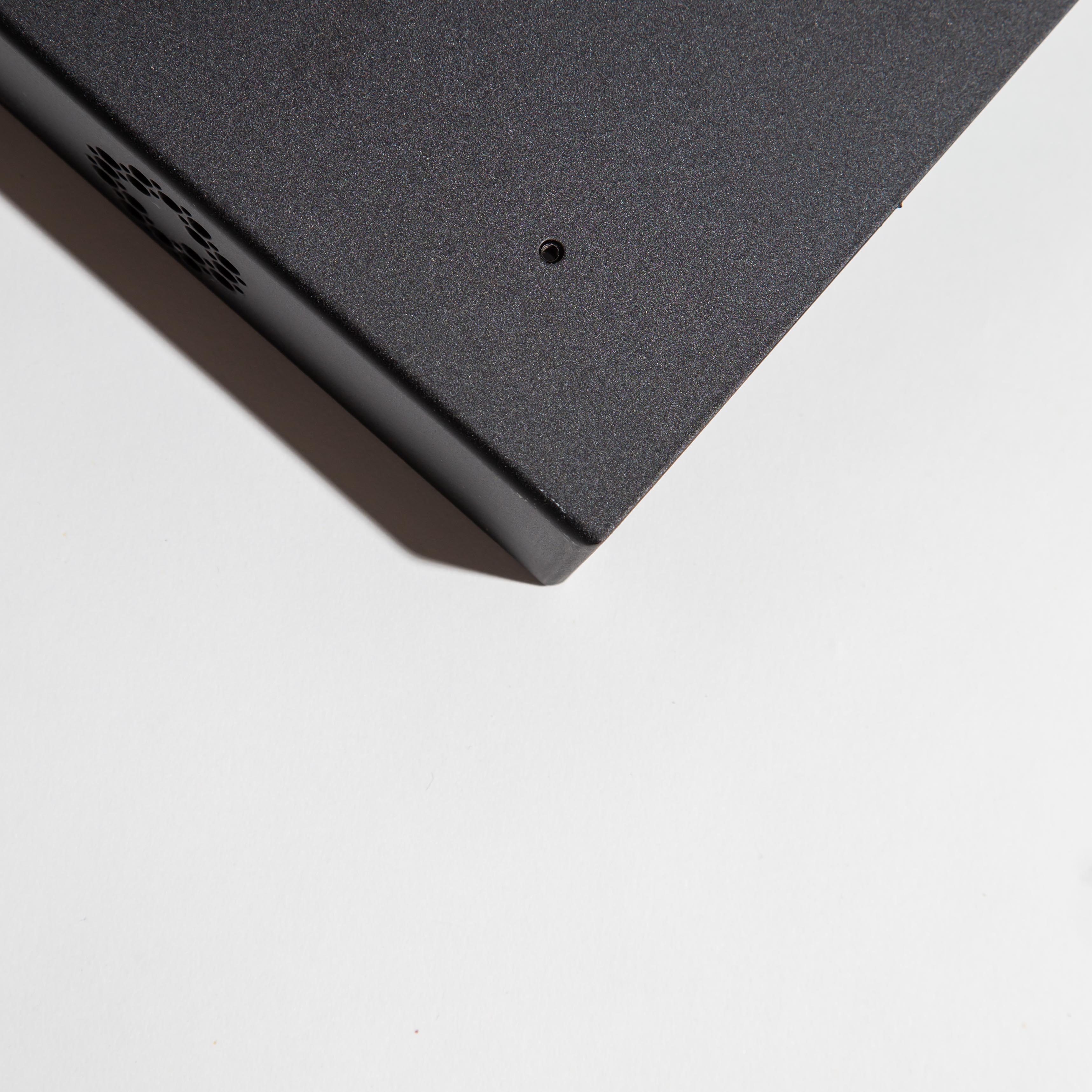 Corner of a black metal box on a white surface with a small hole and vent.