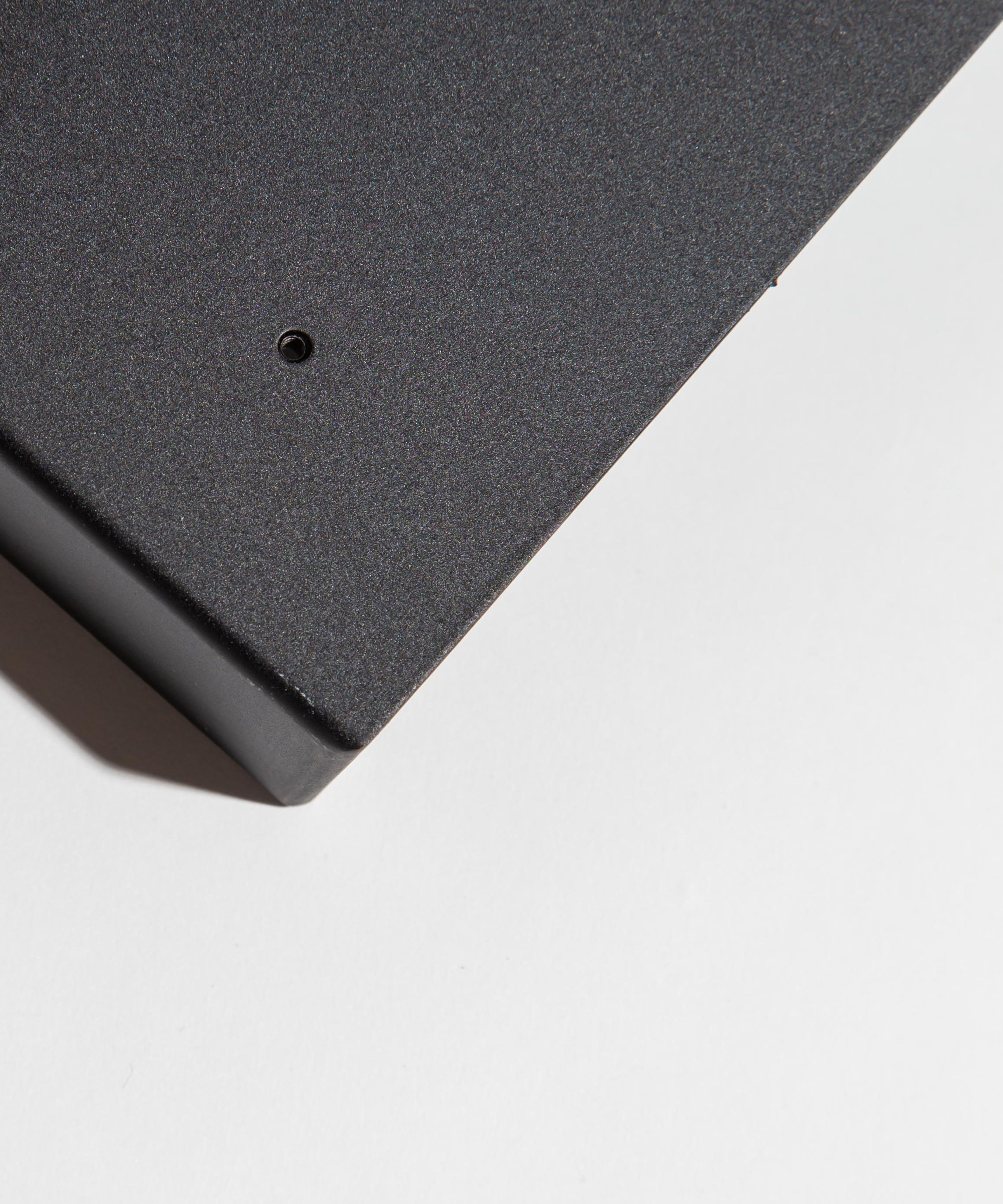 Corner of a black metal box on a white surface with a small hole and vent.