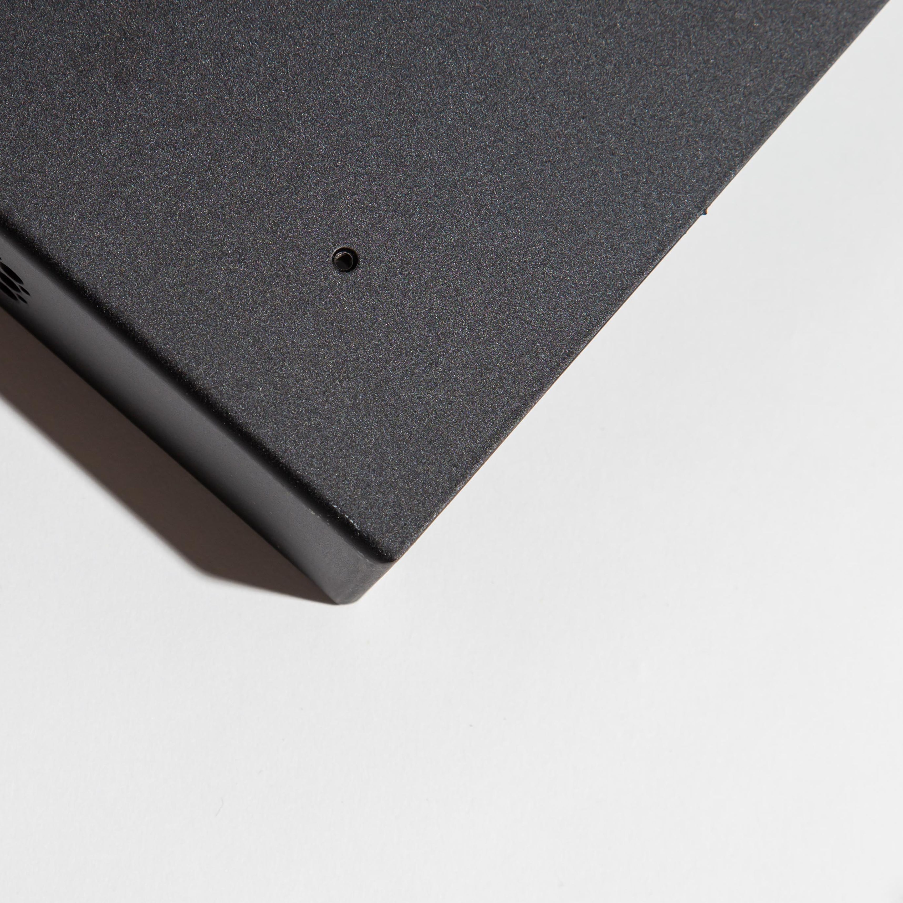 Corner of a black metal box on a white surface with a small hole and vent.