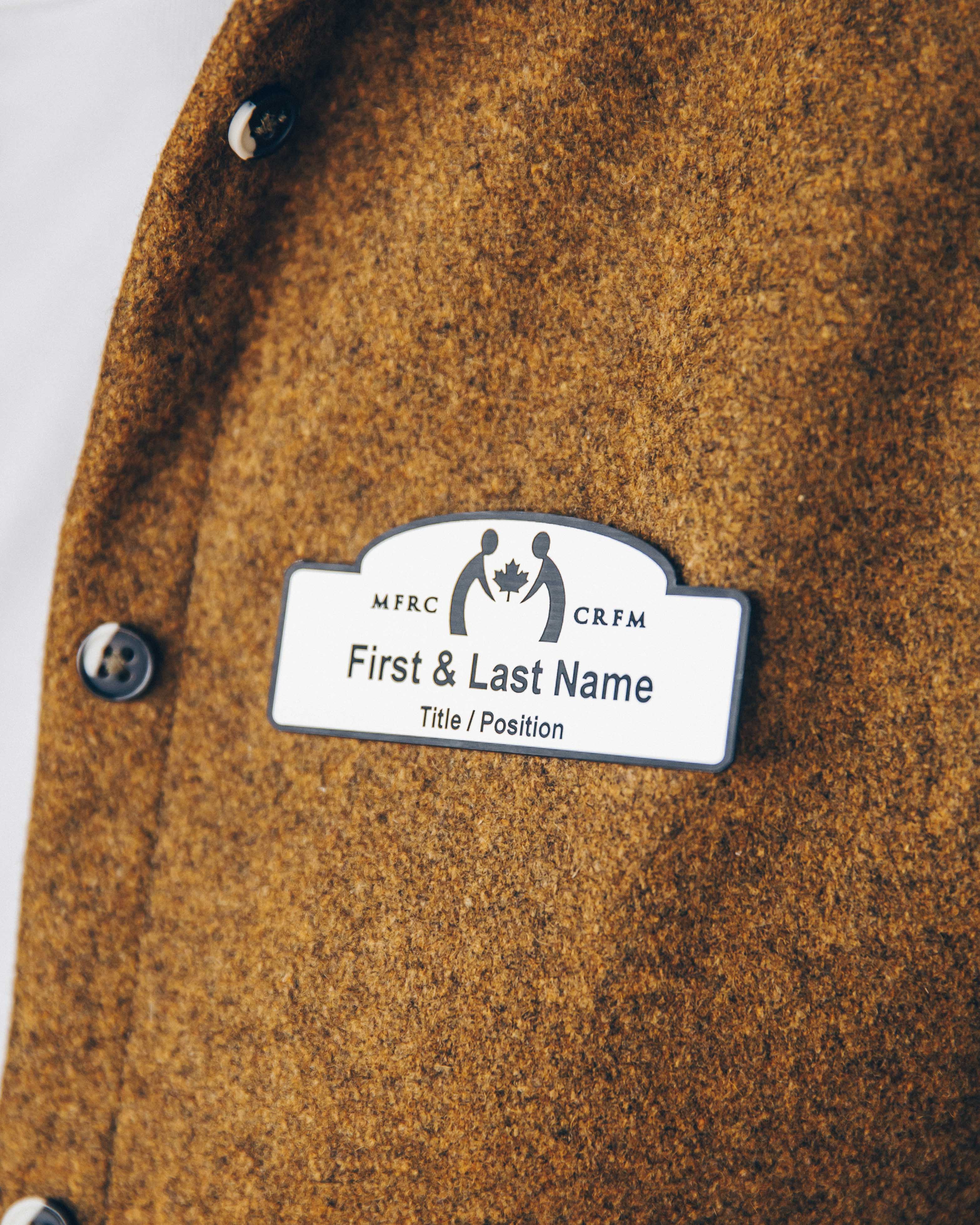 Close-up of a name tag on a brown wool jacket with buttons.