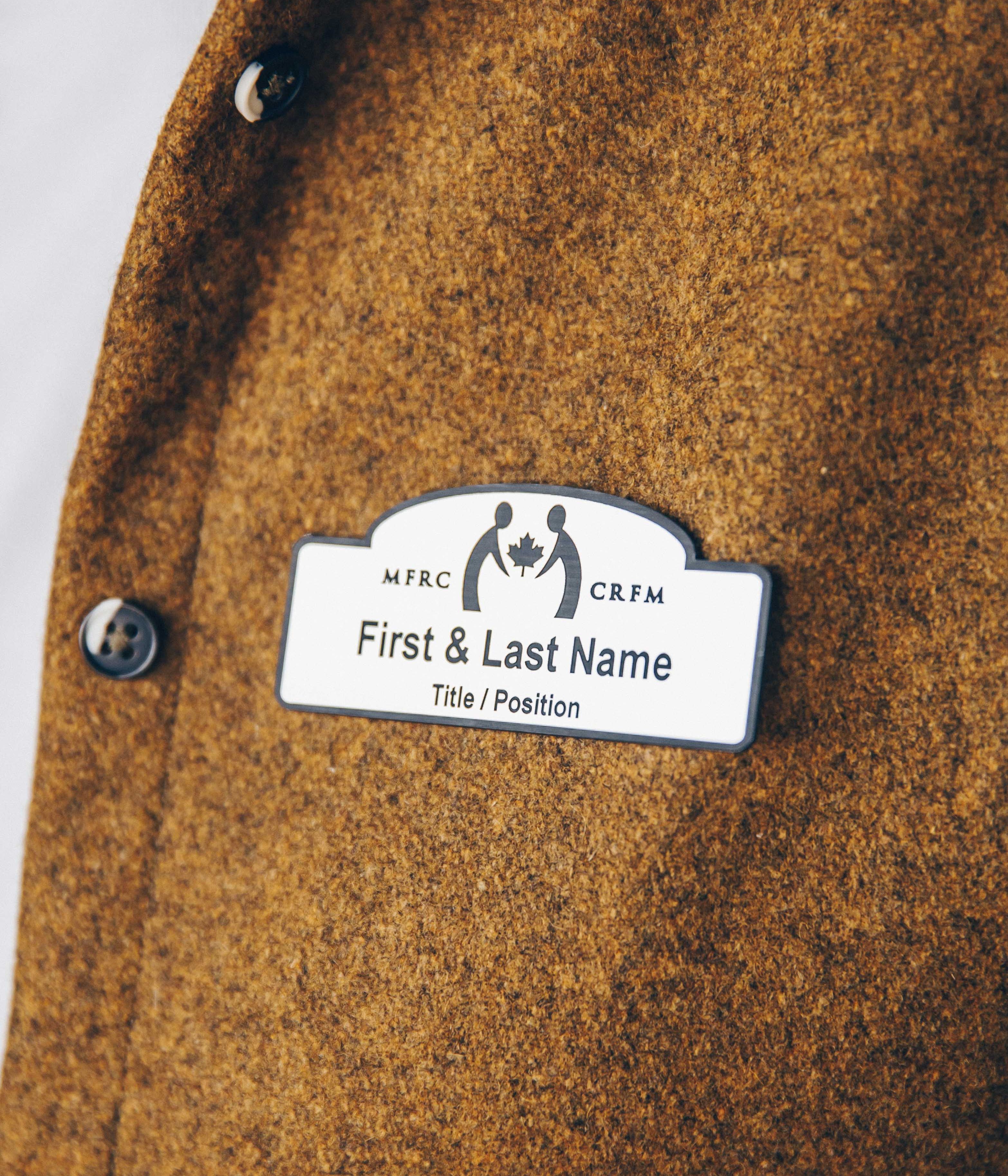 Close-up of a name tag on a brown wool jacket with buttons.
