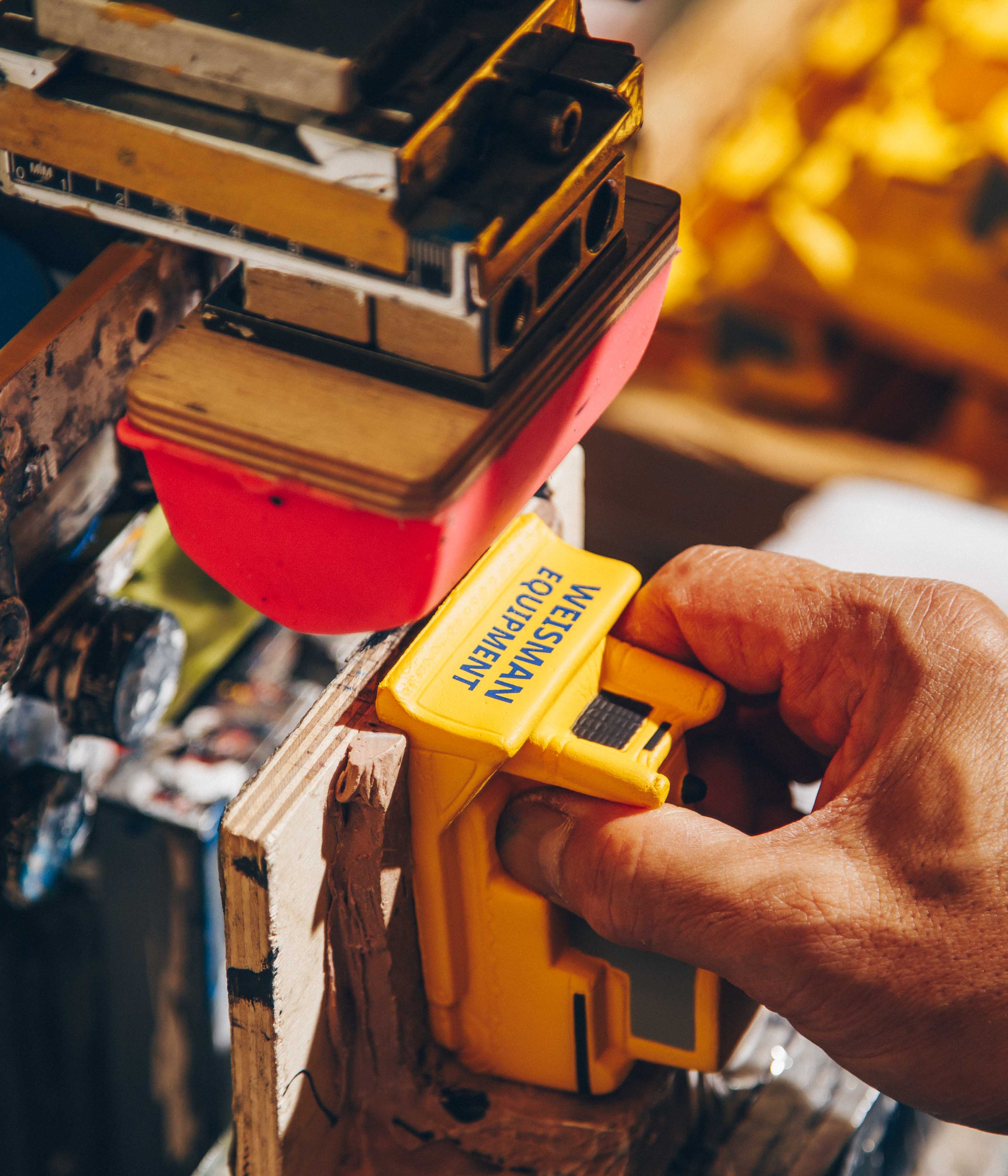 A worker uses a pad printing machine to brand a yellow plastic product labeled "Wesmann Equipment." The setup includes a red silicone transfer pad and a detailed industrial work environment for custom branding.