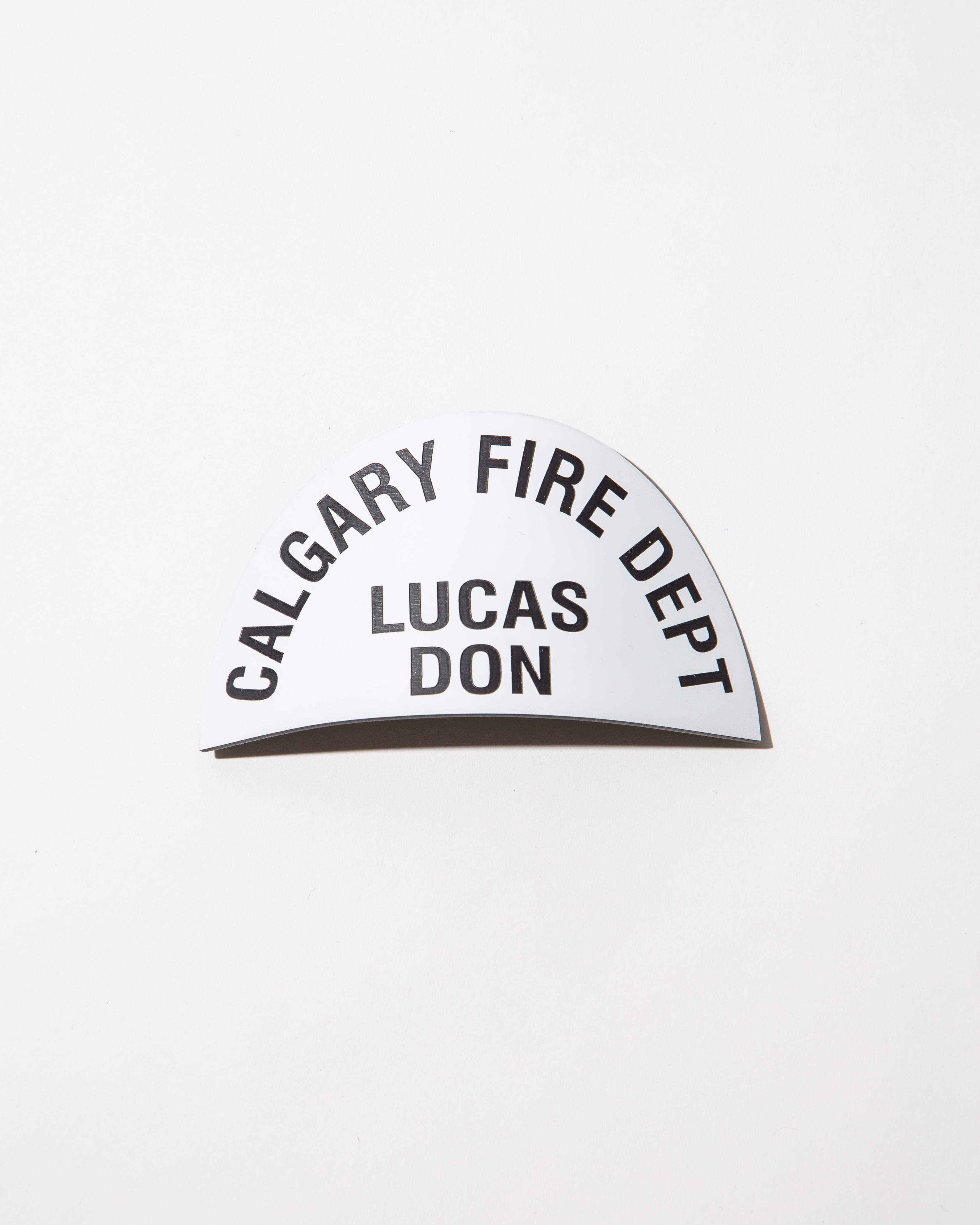 Curved name tag with 'Calgary Fire Dept' and 'Lucas Don' printed in black on white background.