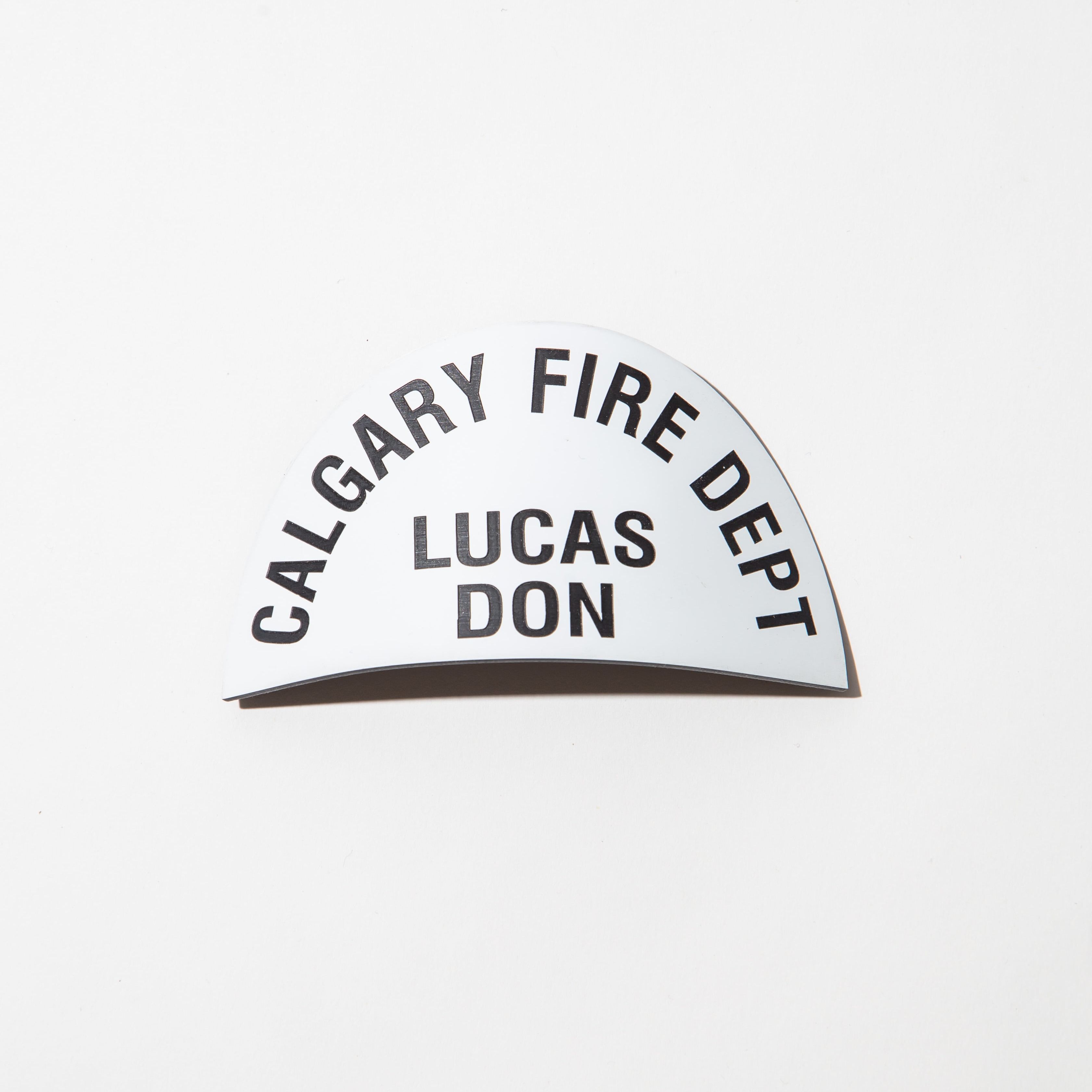 Curved name tag with 'Calgary Fire Dept' and 'Lucas Don' printed in black on white background.